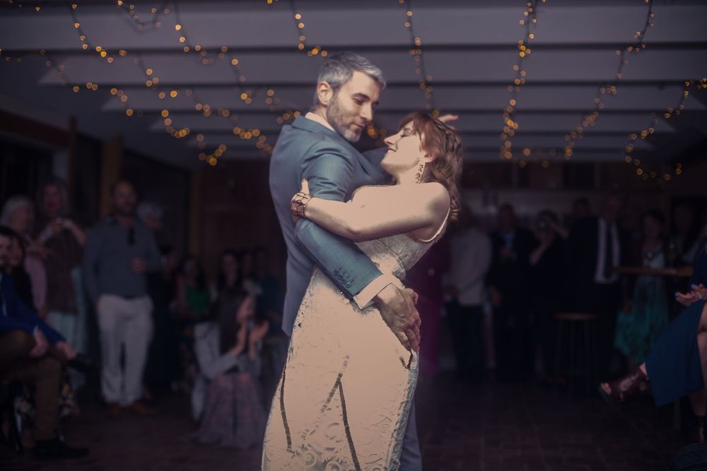A couple shares a romantic slow dance at a wedding reception under twinkling string lights.