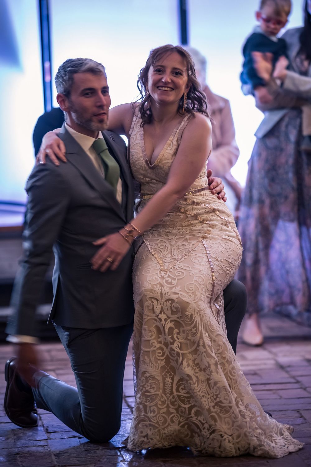 A couple shares a joyful moment on the dance floor at their wedding reception, with the bride wearing a detailed lace gown.
