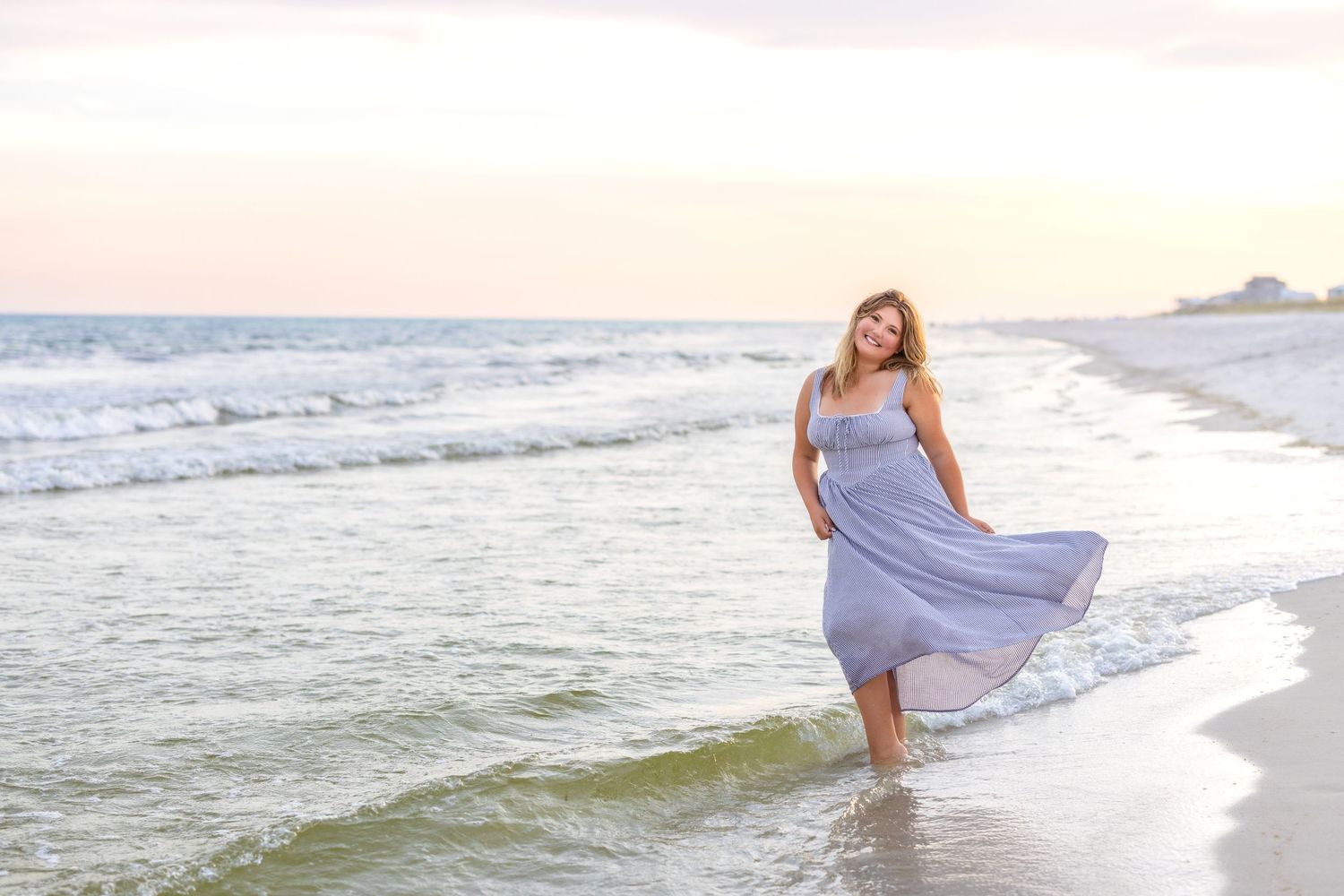 People in light blue dresses pose along a scenic beach at sunset with waves and sand in the background.