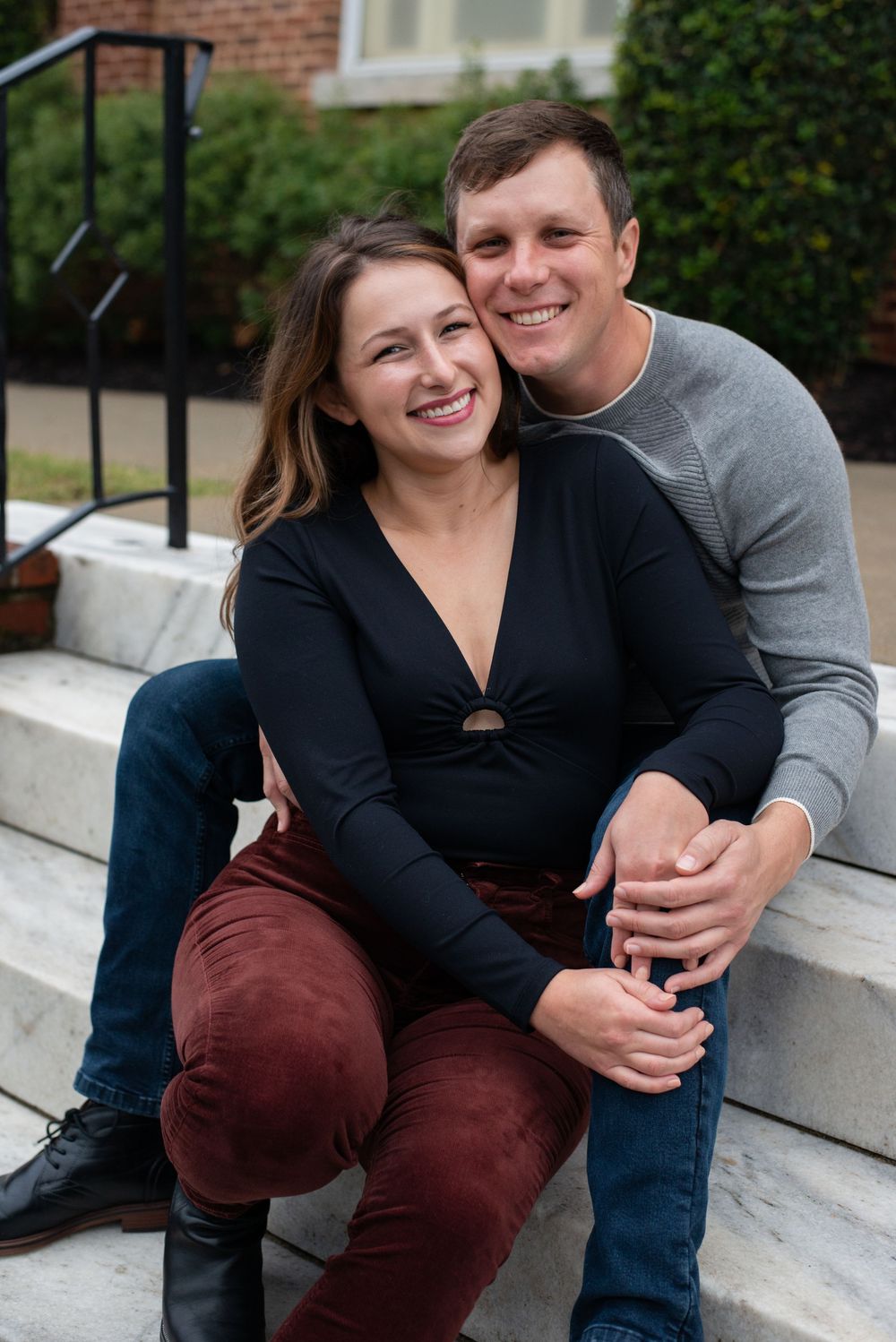 A couple sits together on white steps in a casual outdoor photo shoot.