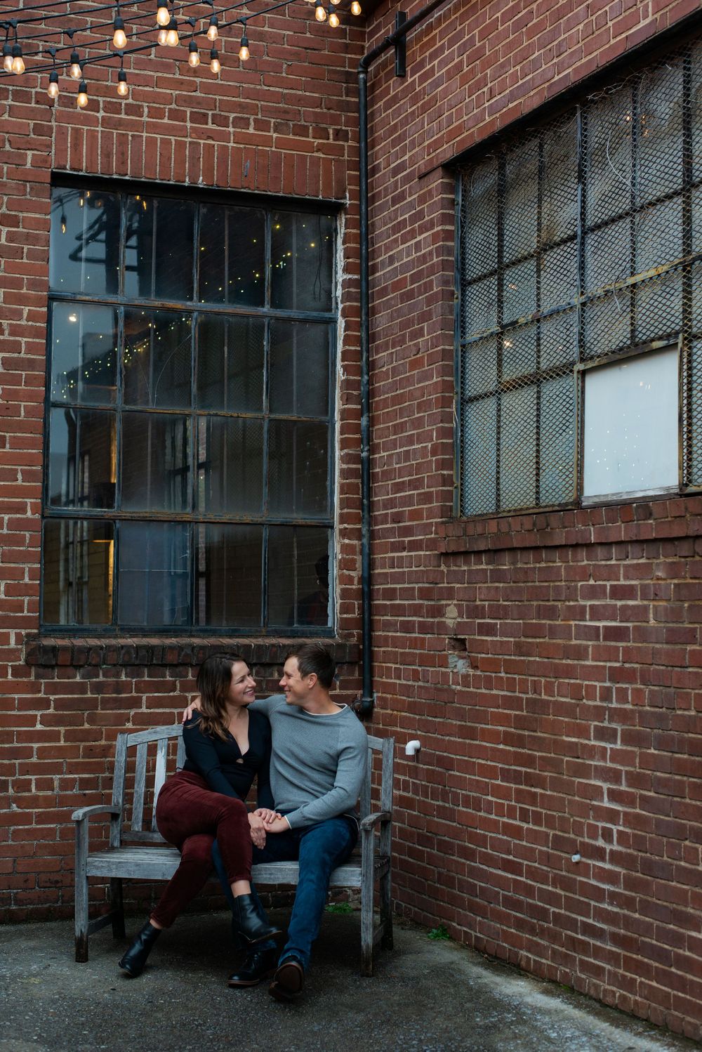 Three progressive shots show a couple sitting on a bench outside a brick building with hanging lights.