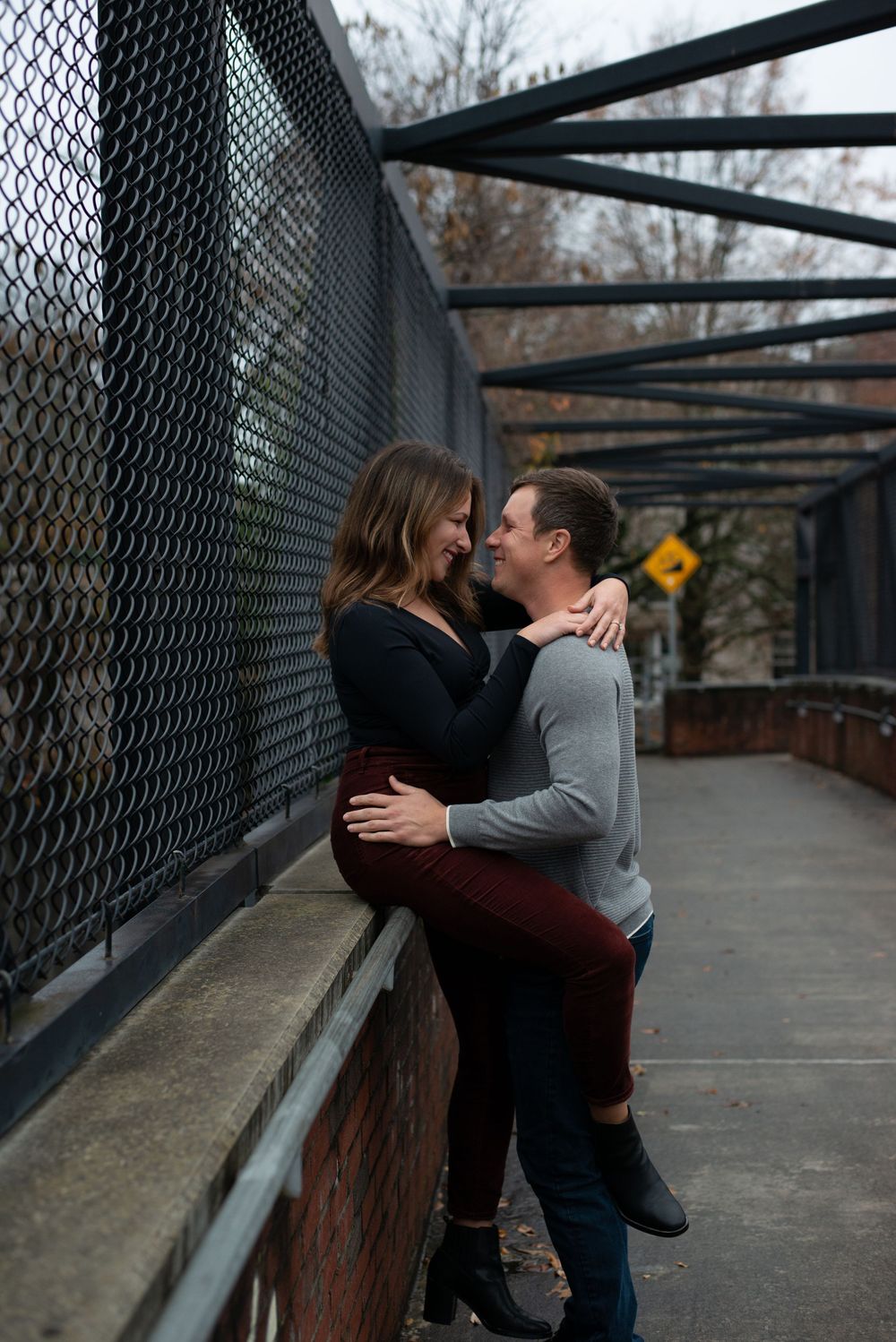 Couple sharing an intimate moment together on a covered bridge walkway with wire mesh railings during autumn.