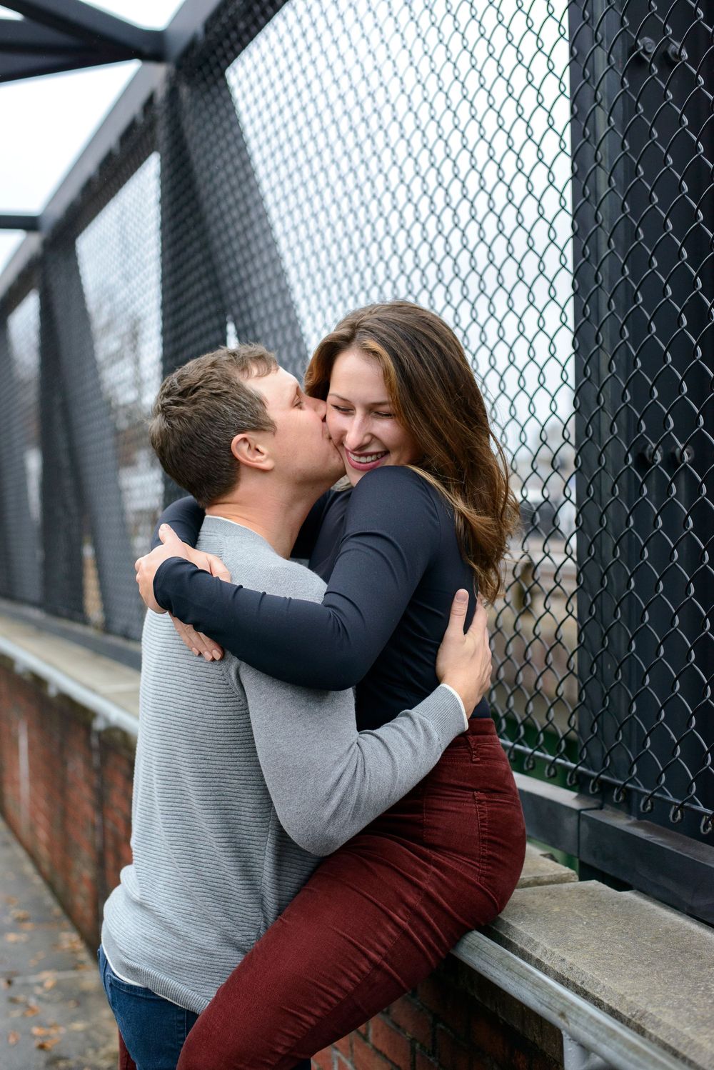 Four sequential photos showing a romantic moment between a couple embracing on a walkway with chain link fence.