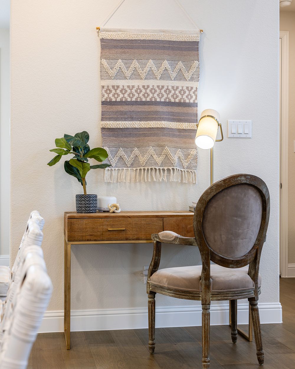 Modern home interior with vintage gray chair, wooden console table, decorative woven wall hanging, and table lamp.