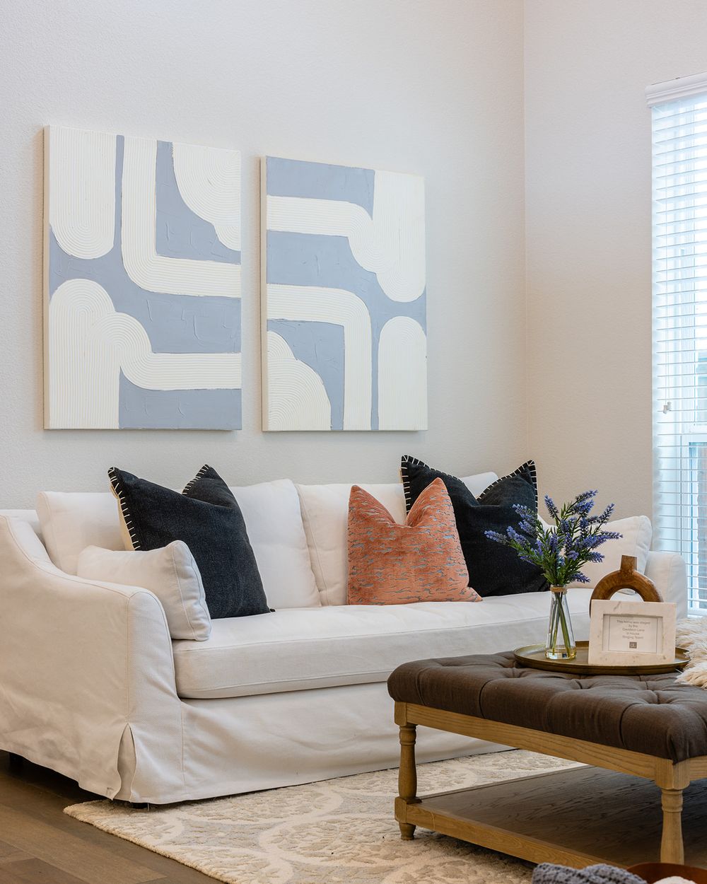 Modern living room with abstract blue and white wall art, white slipcovered sofa, and decorative pillows.