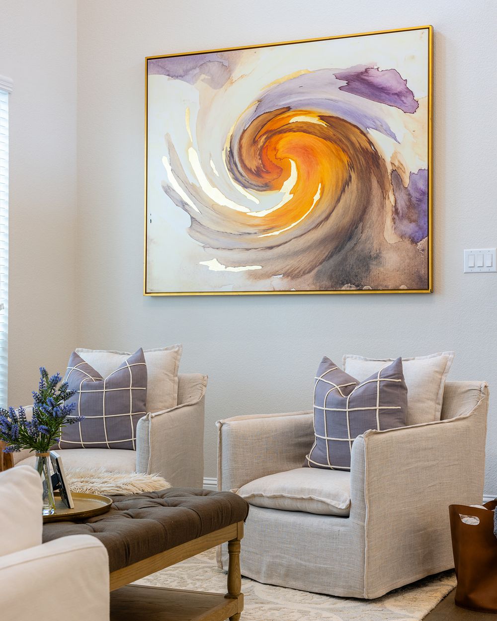Modern living room with abstract orange and purple spiral artwork above gray accent chairs and decorative pillows.