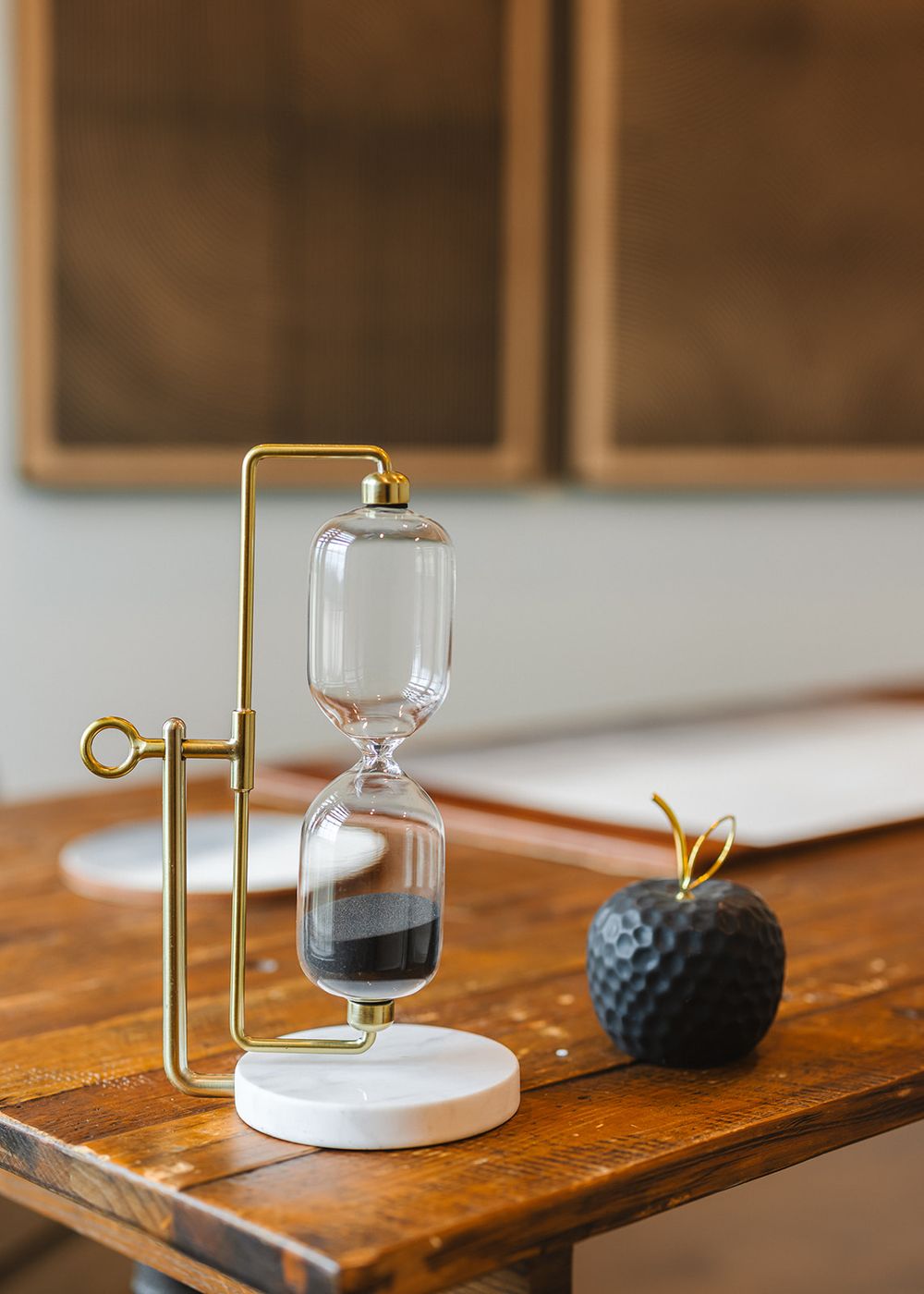 Wooden display table showcasing modern hourglass and geometric decorative objects with gold metallic accents.