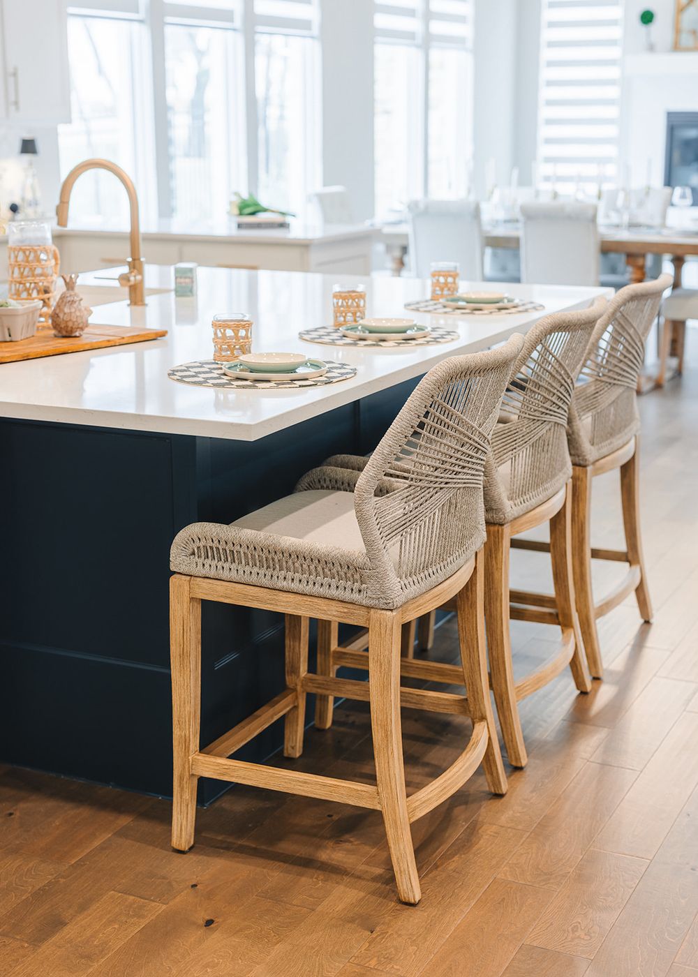Modern kitchen island features elegant woven rattan counter stools and gold accents with a light hardwood floor.
