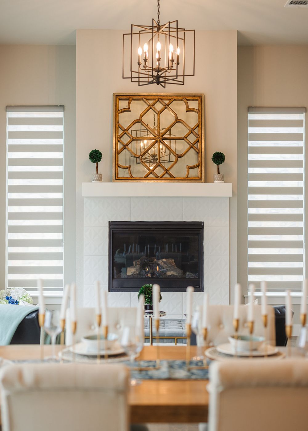 Modern dining room features geometric chandelier, zebra pattern window shades, and elegant table settings with gold accents.