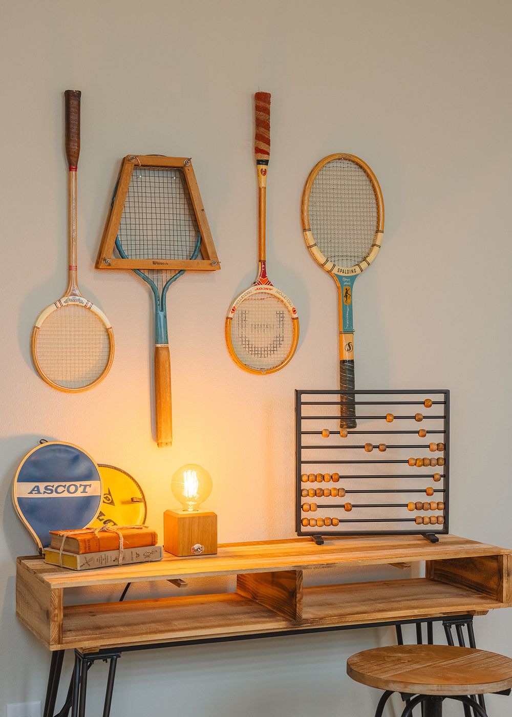 Vintage tennis and badminton rackets displayed on wall above wooden console table with abacus and retro sports items.