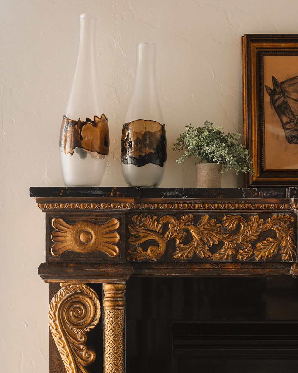 Two white ceramic vases with natural burnt details sit atop an ornate gold-trimmed fireplace mantel with carved designs.