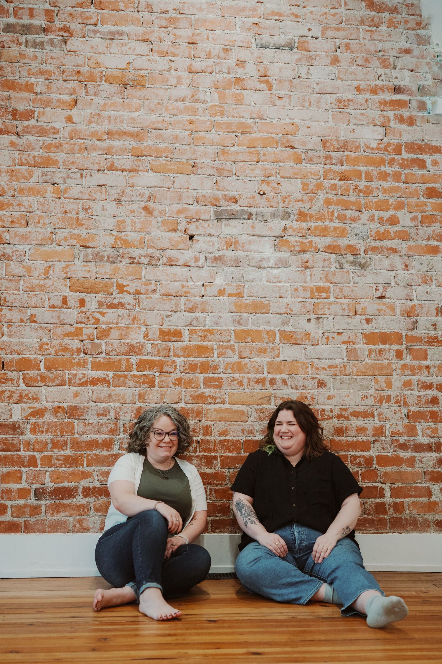 Four connected photos show two people sitting casually against exposed brick wall in a minimalist indoor setting.