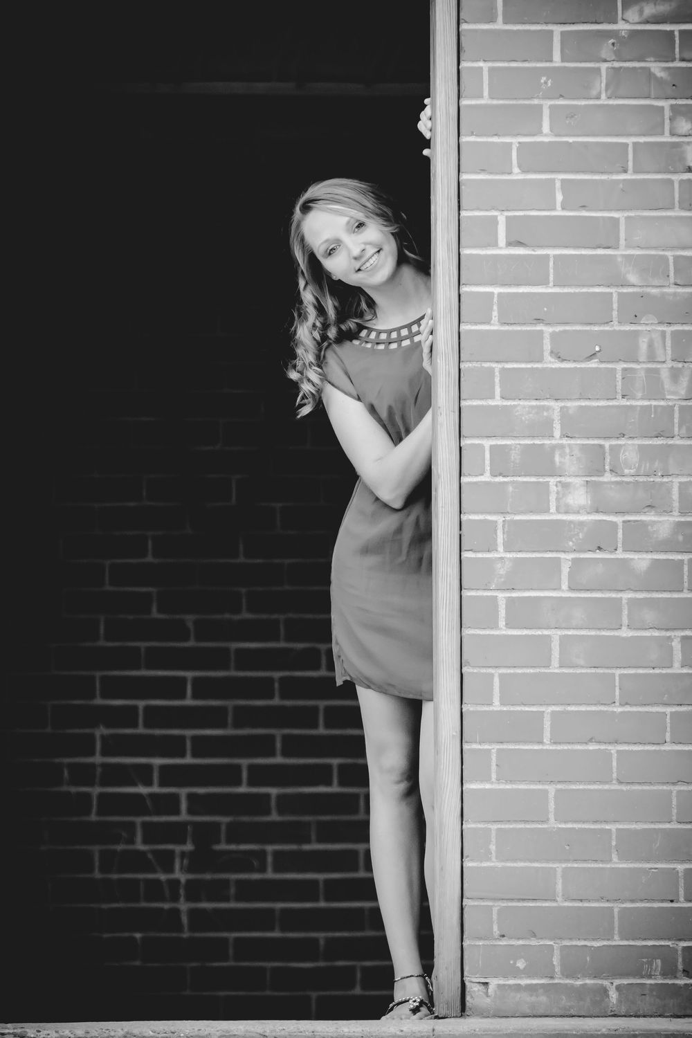 Black and white artistic photo series showing someone playfully peeking around a brick corner in a dress.