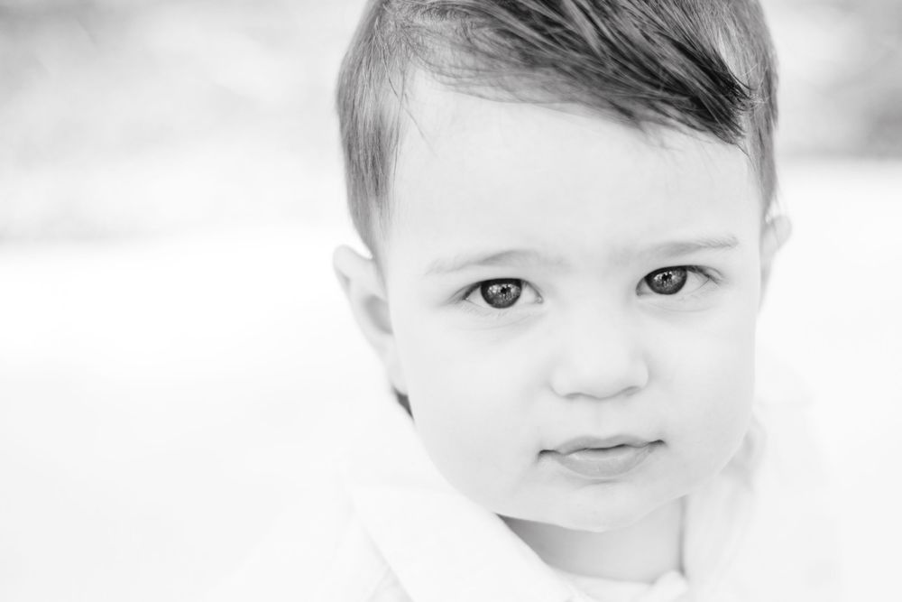 A black and white high key portrait with soft lighting showcases gentle features and pale eyes against a bright background.