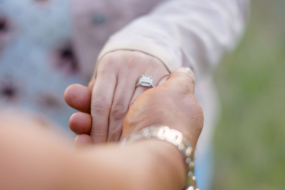 A close-up view of people holding hands with an engagement ring prominently displayed.
