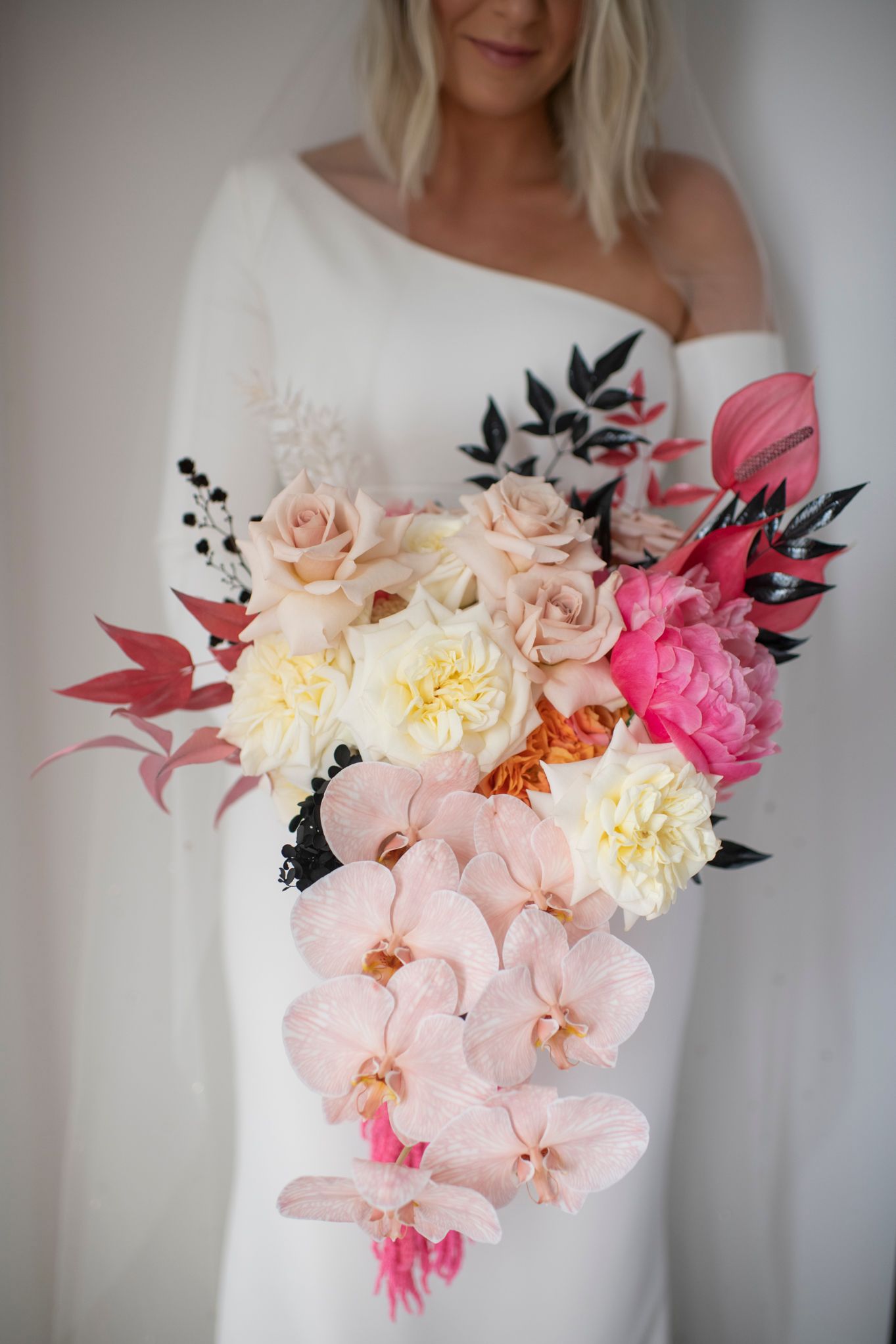 Close-up of a white wedding dress adorned with cascading pink orchids, peach roses, and black floral accents.