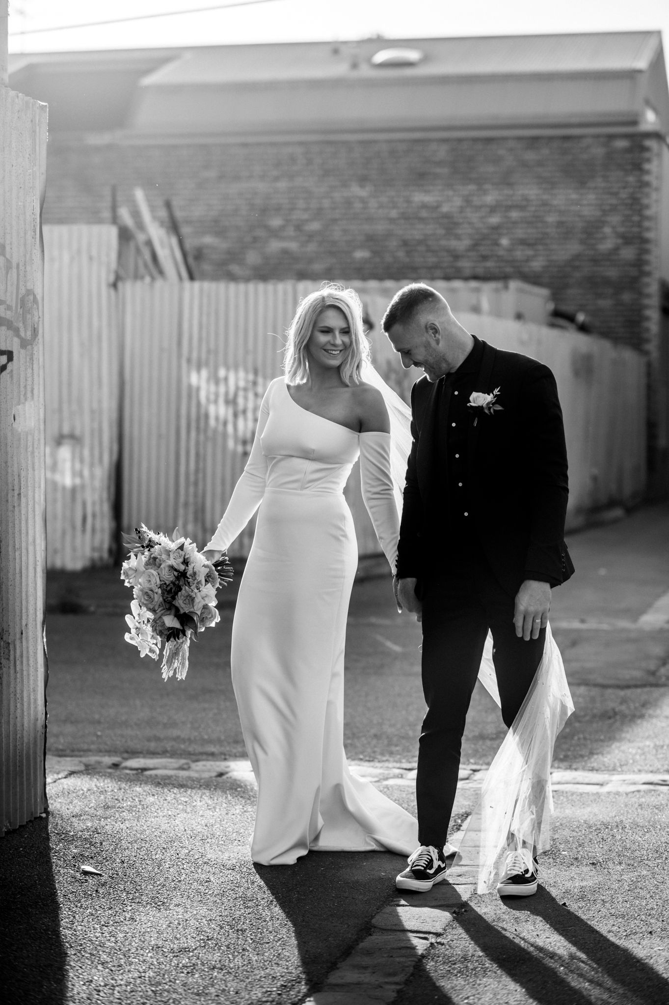 A couple on their wedding day walking together outdoors in black and white, she in white gown and he in dark suit.