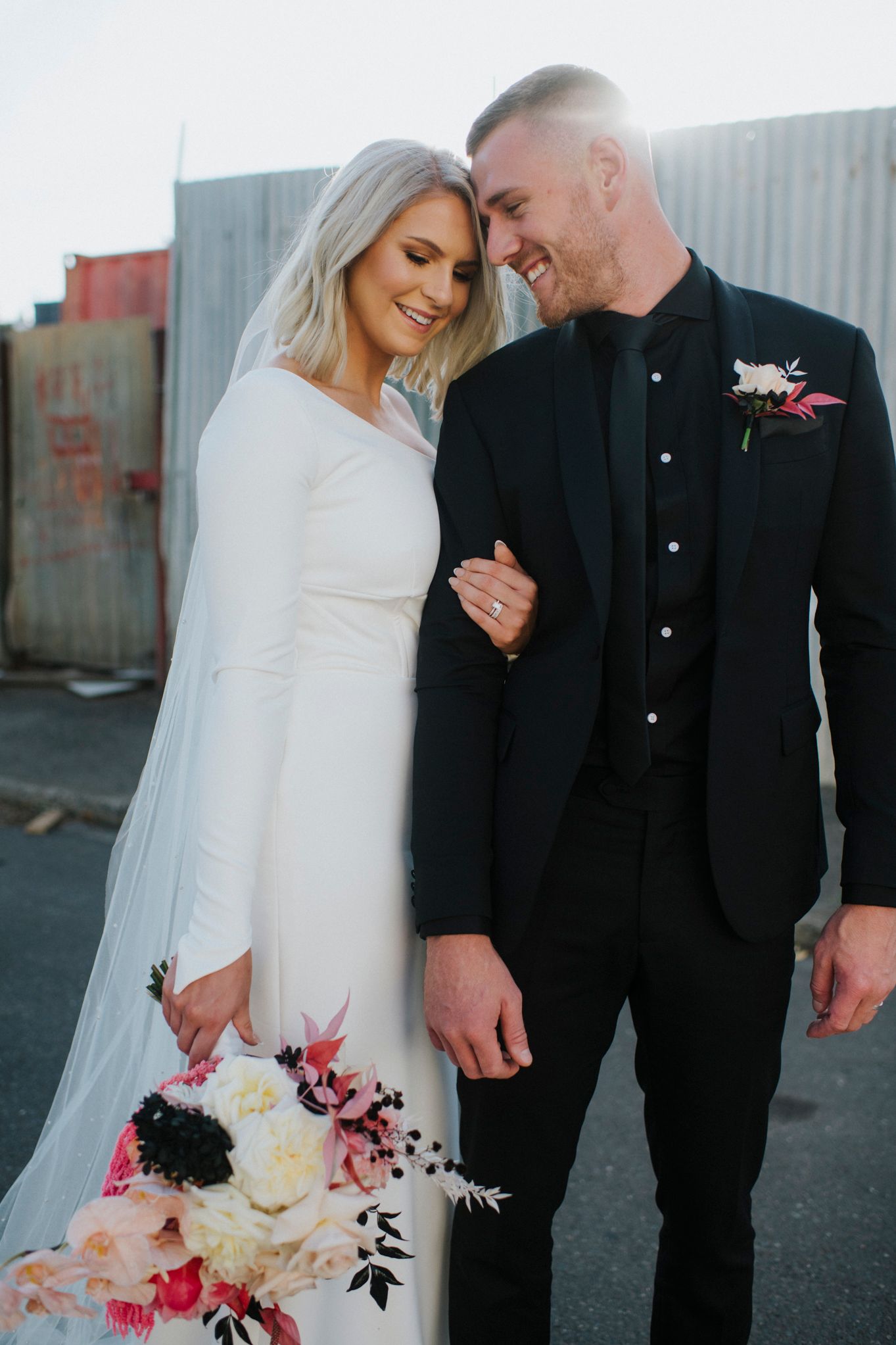 A couple in wedding attire share an intimate moment, with the bride in white holding a pink and white floral bouquet.