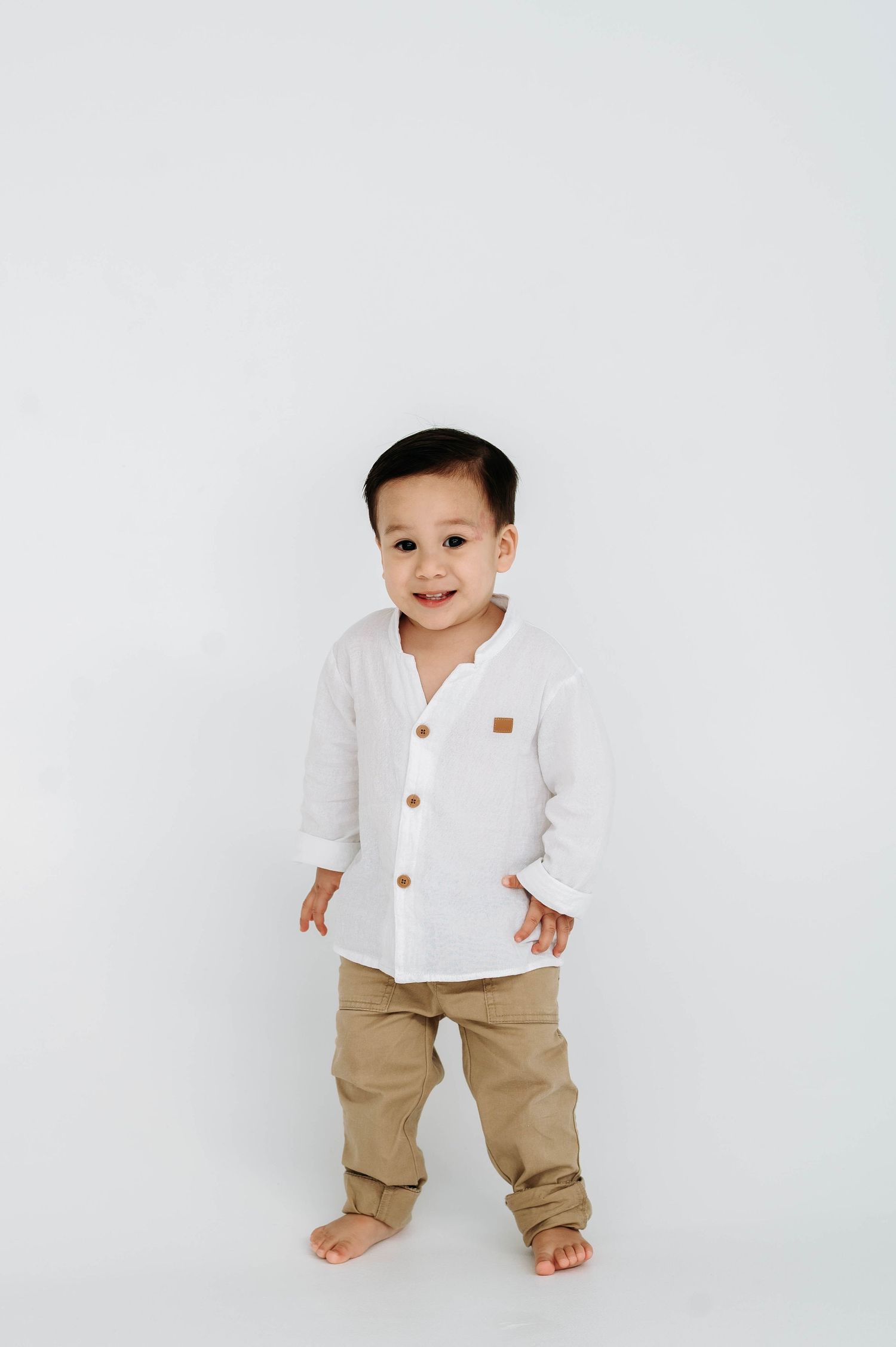 Small child in white button-up shirt and khaki pants standing against white background.