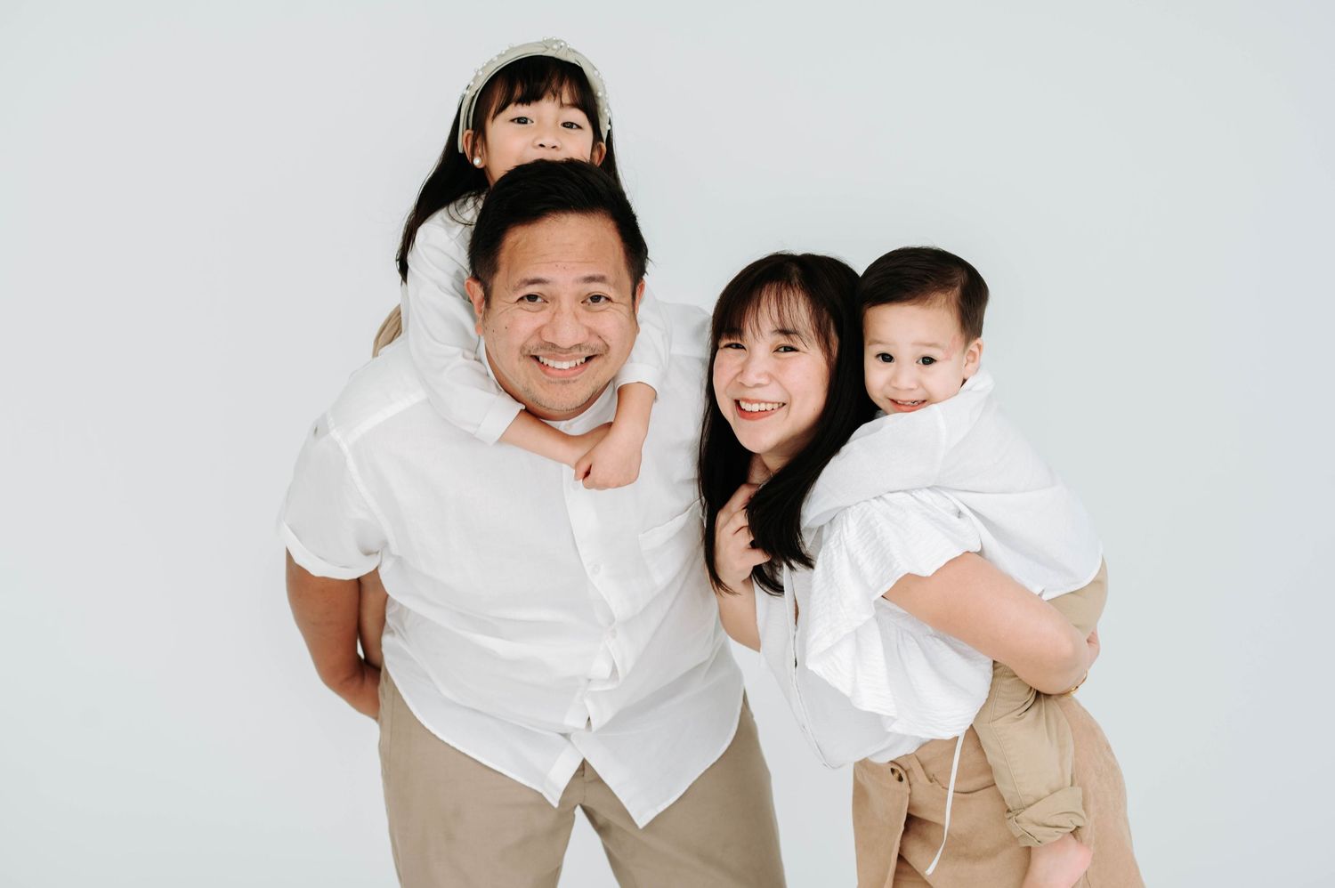 A cheerful family wearing matching white shirts and khaki pants posed together against a light background.