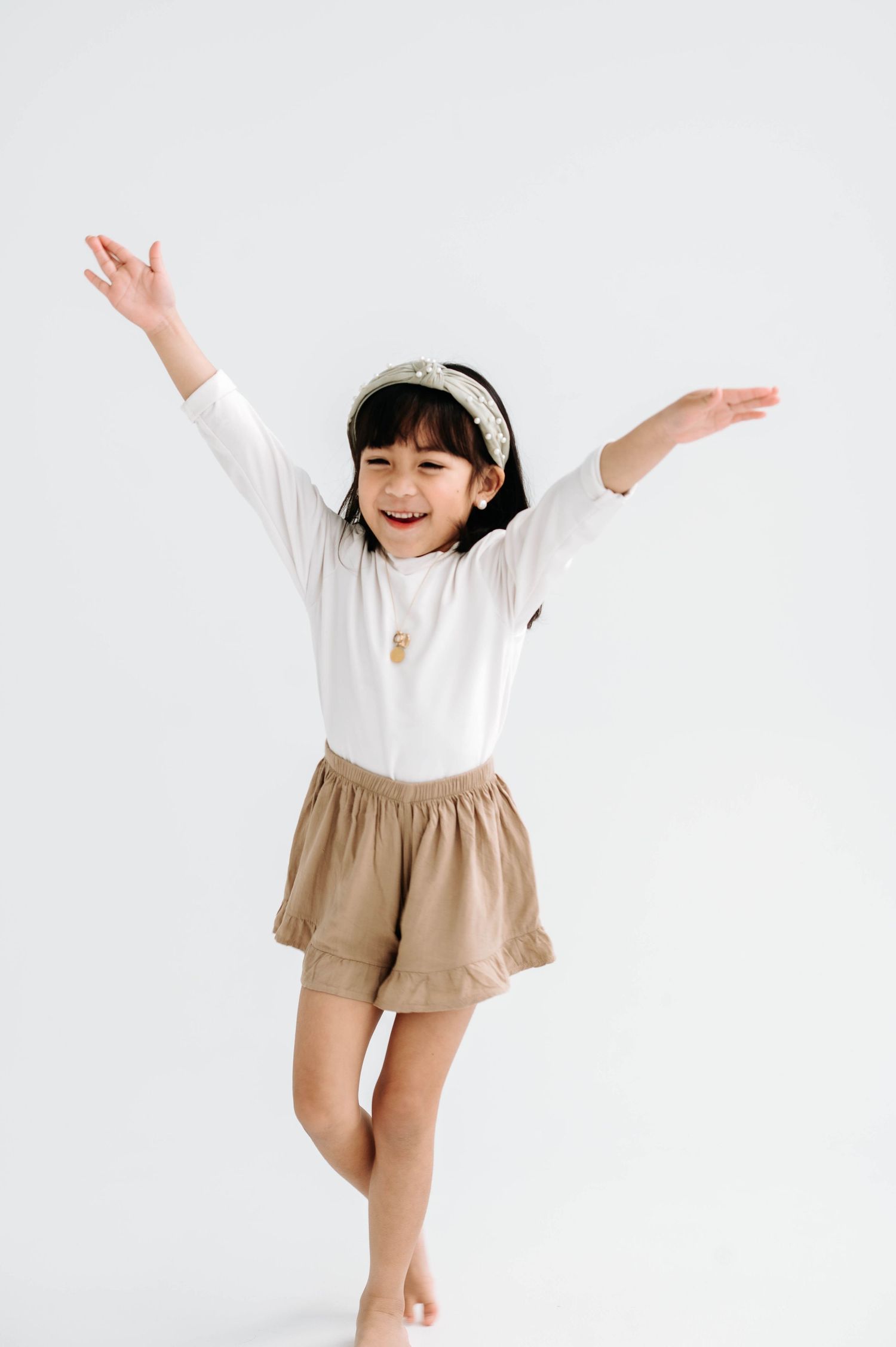 Young girl in white shirt and beige shorts jumps joyfully against white background.
