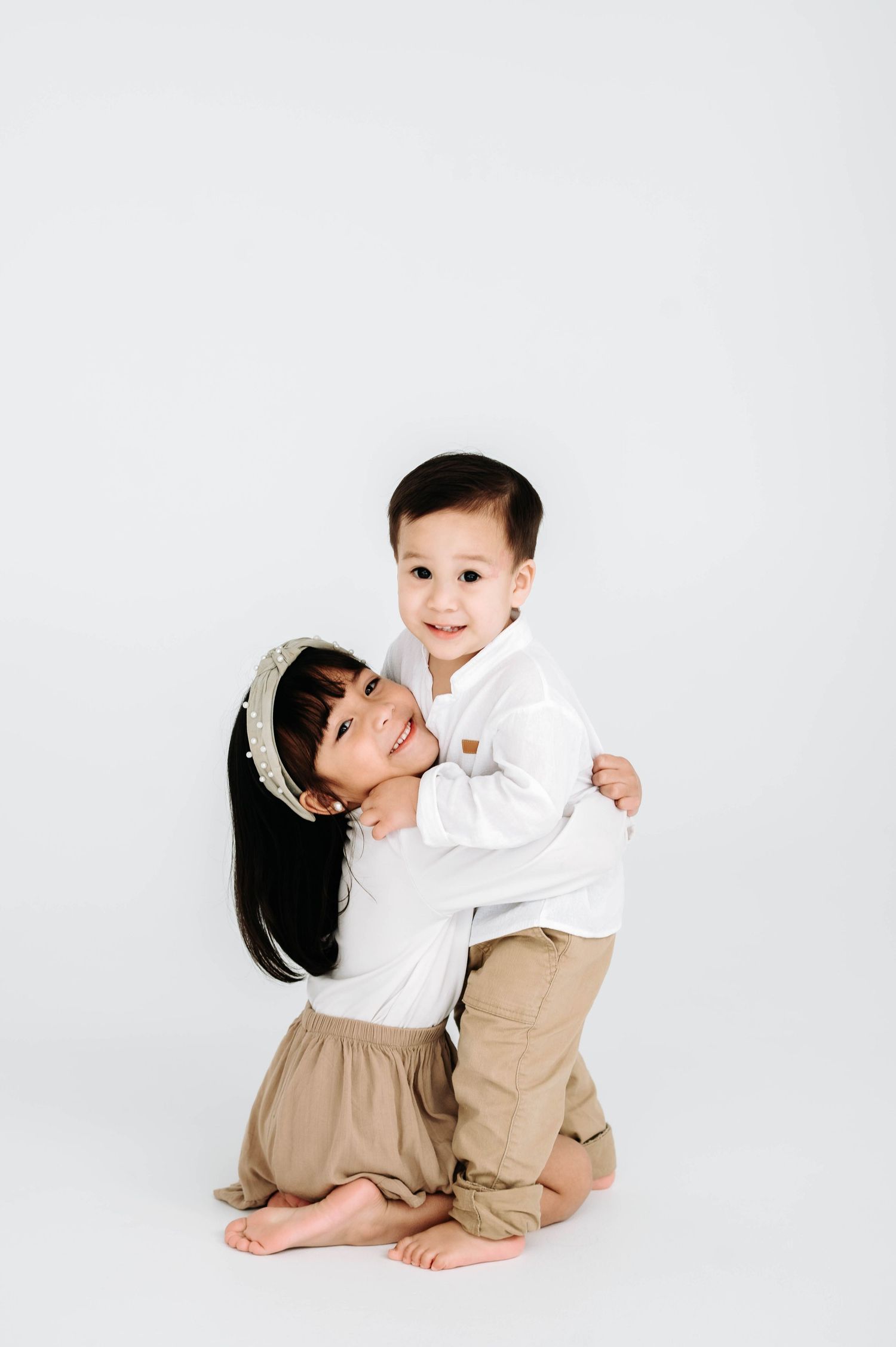 Two young children in matching white and khaki outfits playing together on white background.