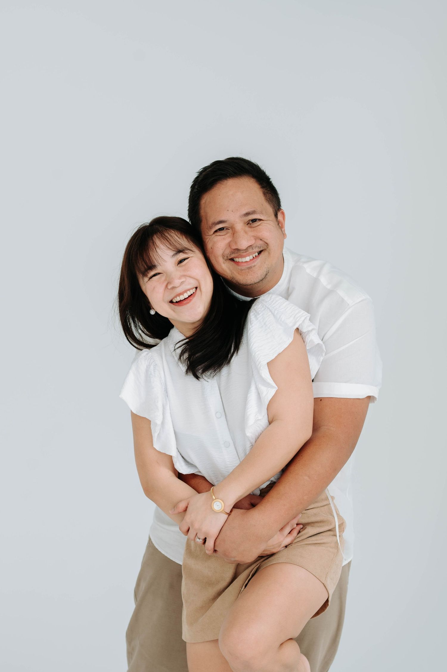 Two people wearing white shirts embrace and laugh together against a light gray background.