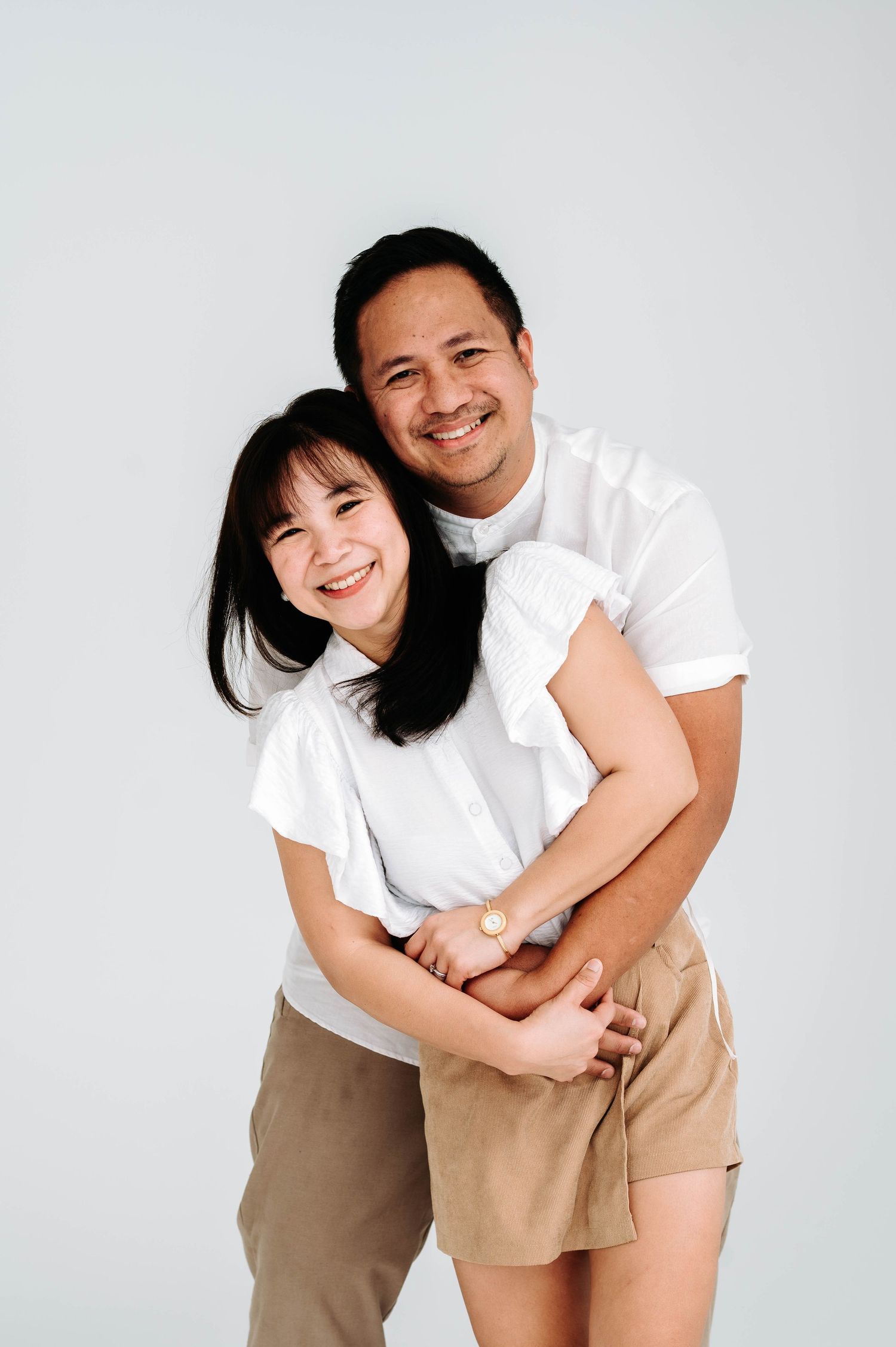 Family members wearing coordinated white shirts and khaki shorts share joyful embraces against a white background.