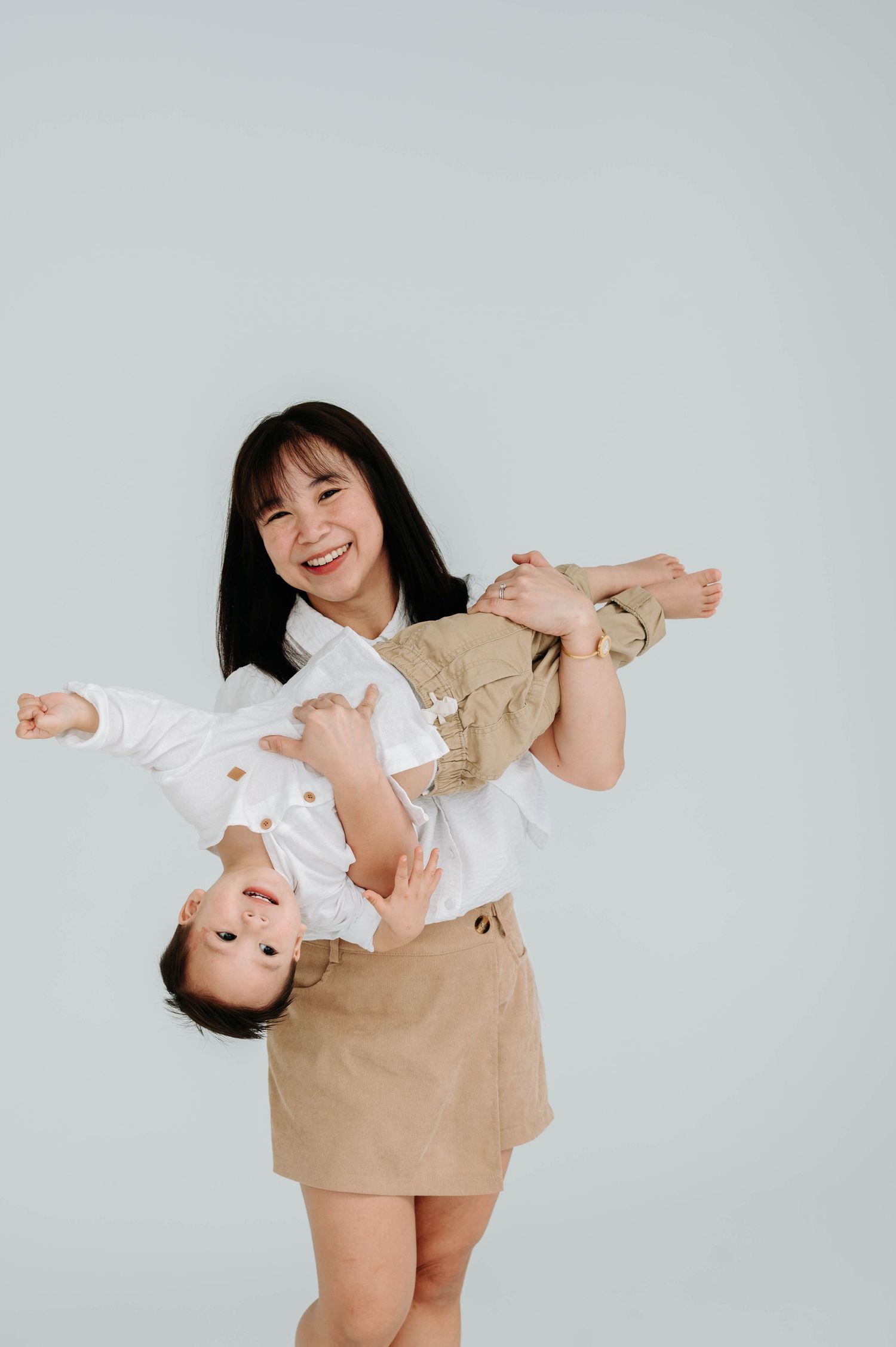 A joyful moment captured as a person playfully holds another upside down against a light backdrop.