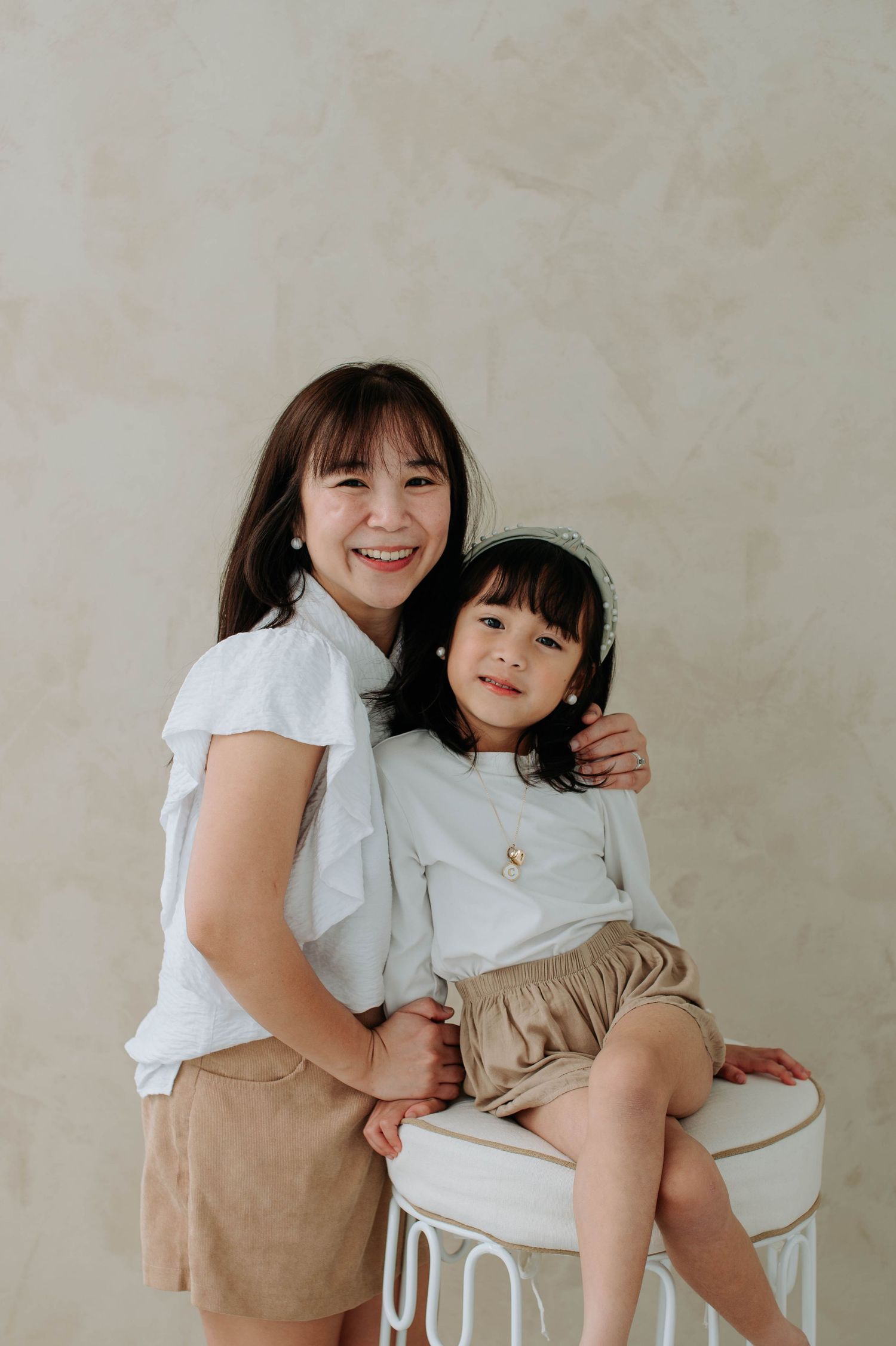 Pair of people in white shirts and khaki bottoms share a joyful moment while sitting on a white stool.