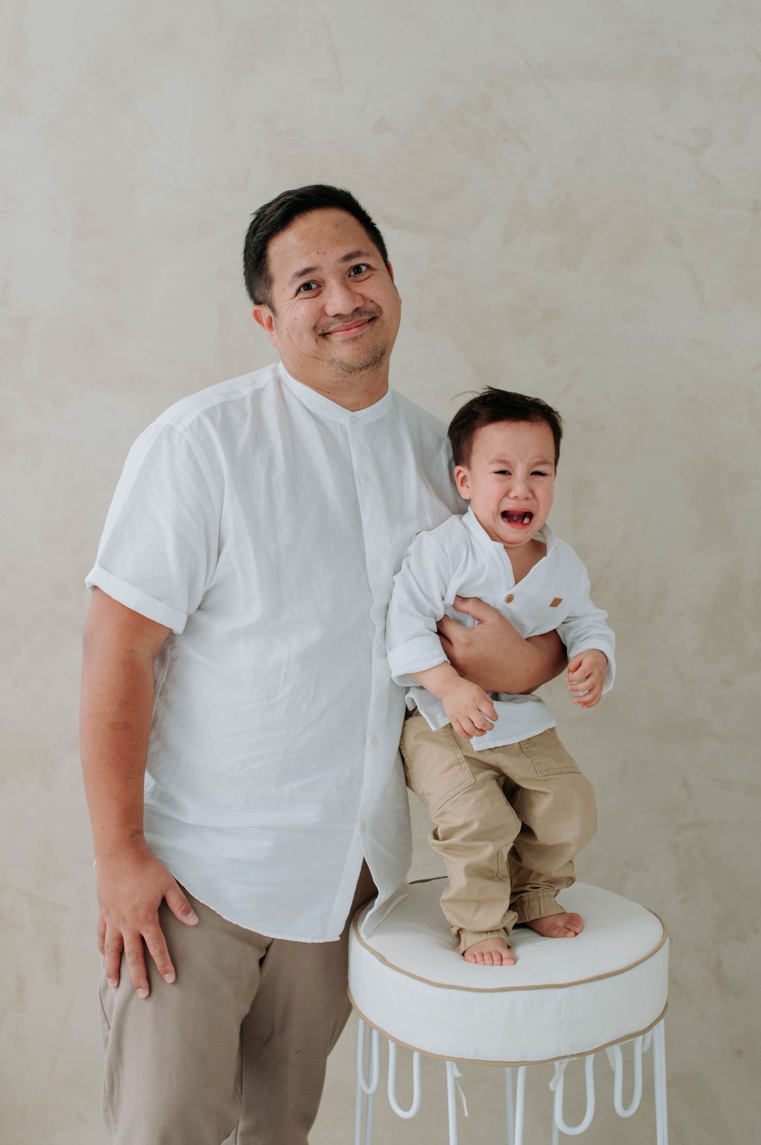 A touching family portrait with two people in white shirts standing by a decorative white stool.