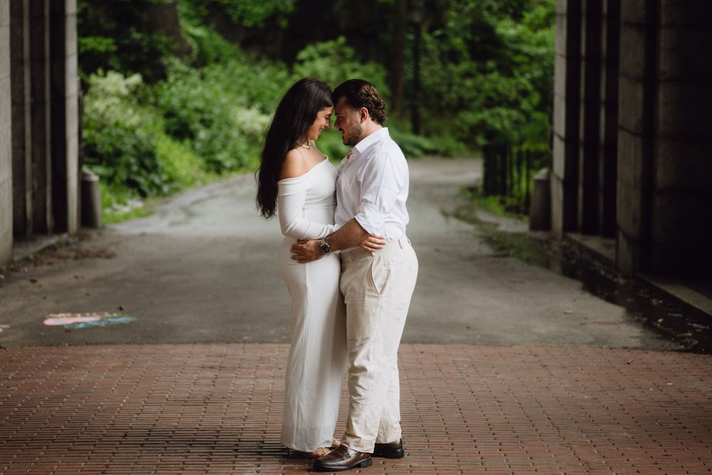 A romantic couple in white attire embrace on a brick pathway under a covered bridge.