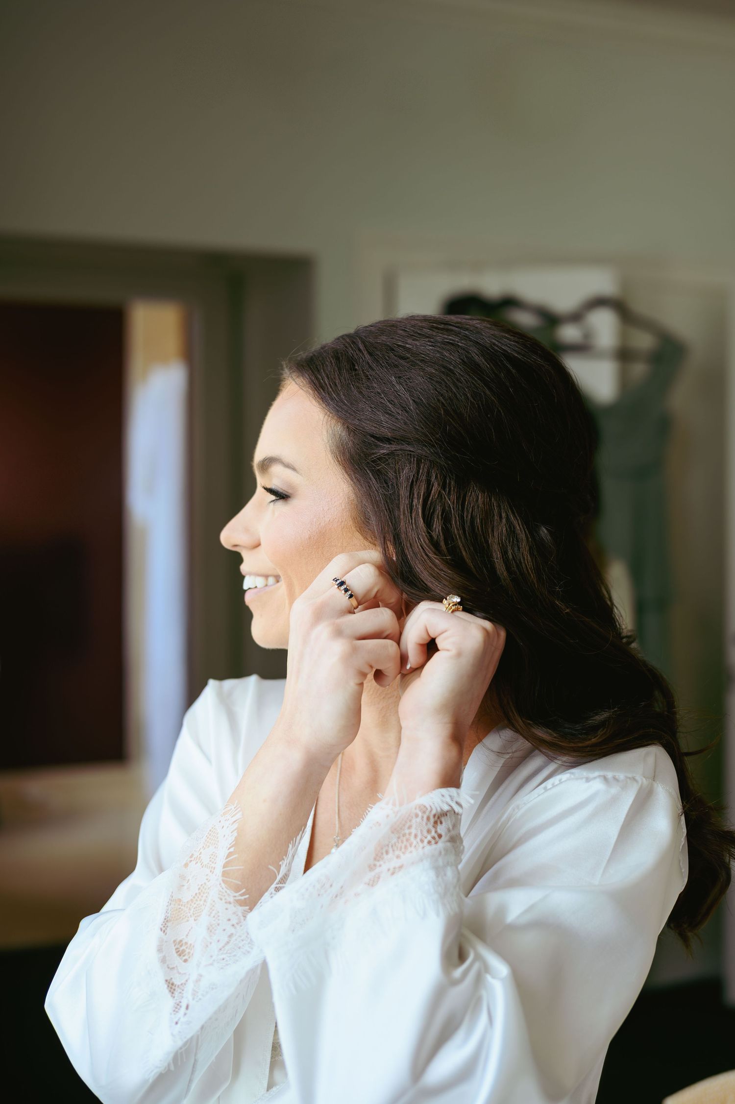 Person in white robe puts on earrings while getting ready in moody interior lighting.