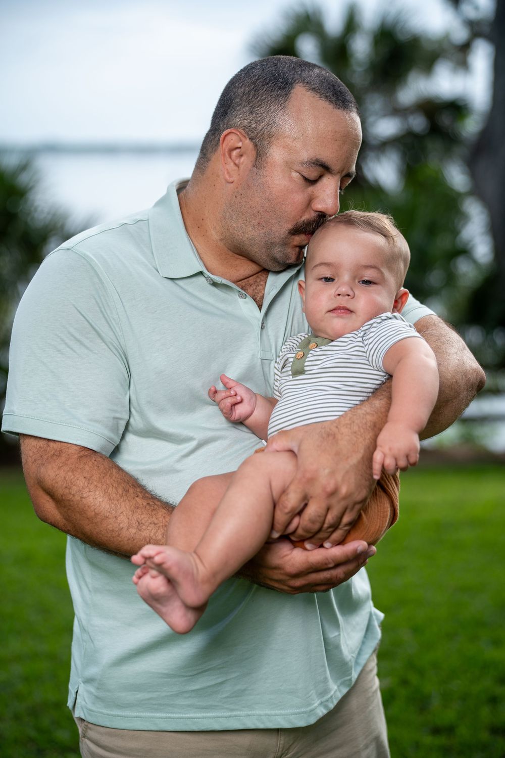Parent holding baby outdoors on grass, playful and tender family moment during Tampa lifestyle photoshoot.