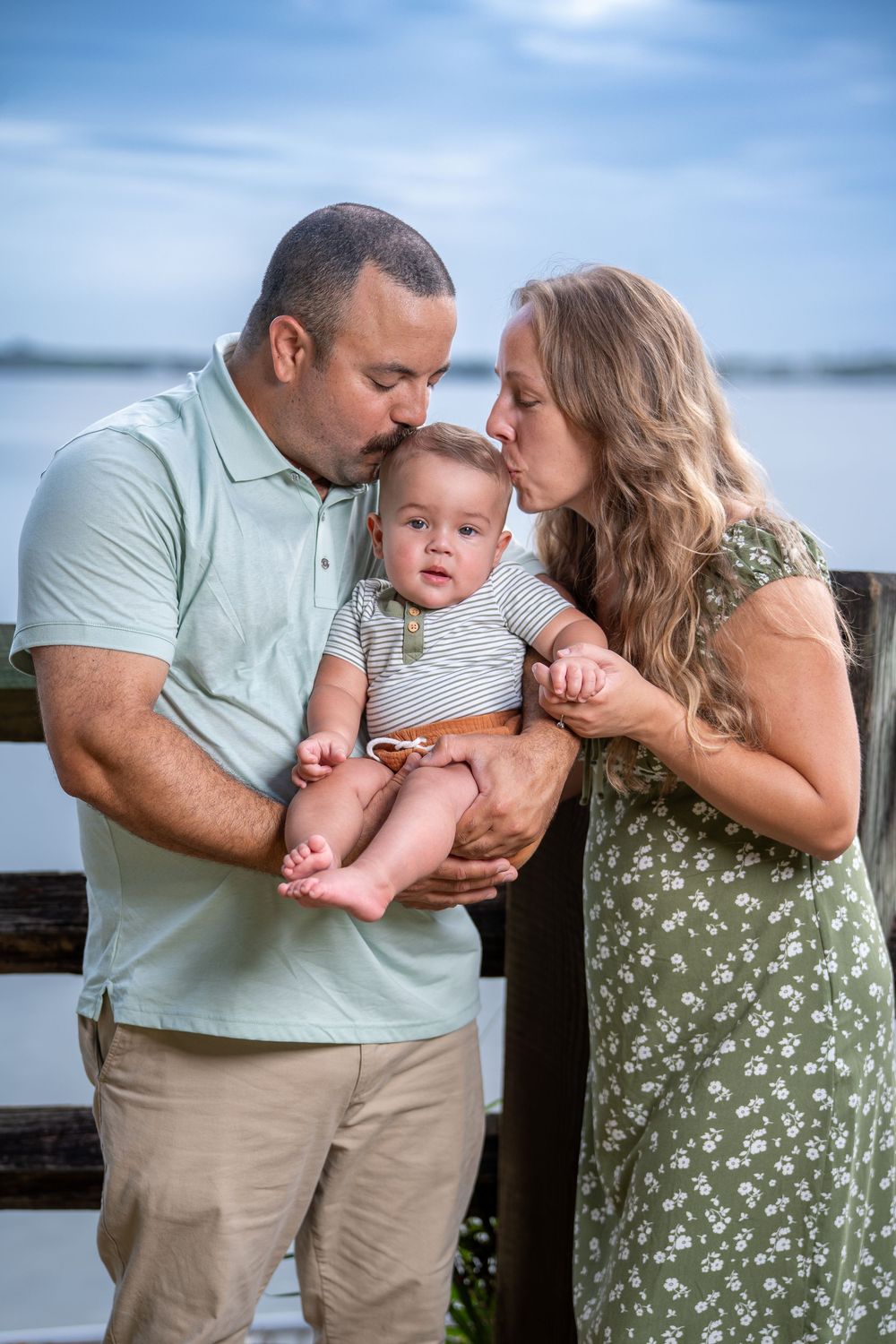 Parents with baby sharing tender moment by the waterfront, matching outfits in green tones — Tampa family photography.