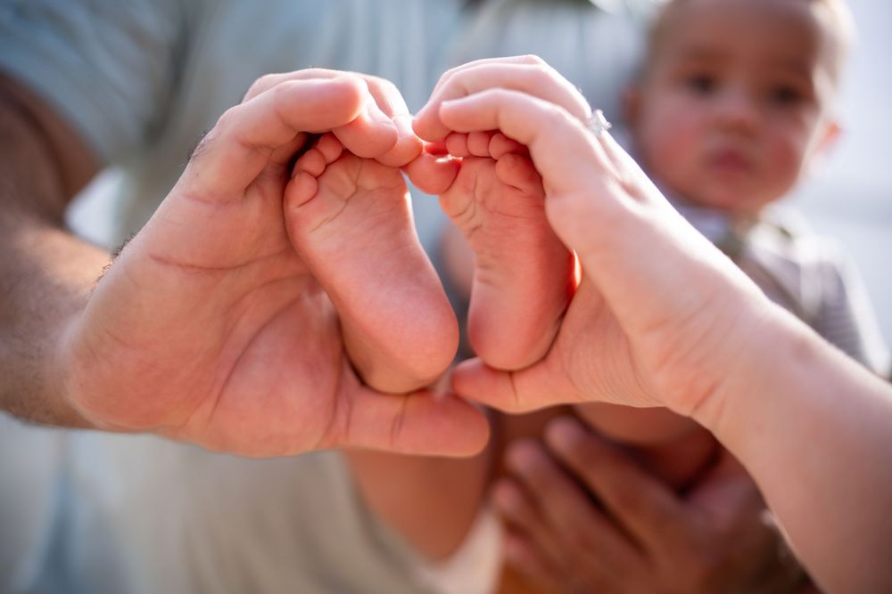 Adult hands forming heart shape with baby’s tiny feet, emotional newborn photography in Tampa, Florida.
