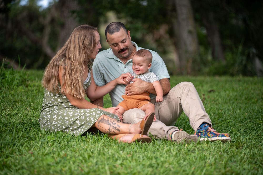 Parents sitting on green grass with baby, joyful outdoor family session in Tampa, Florida.
