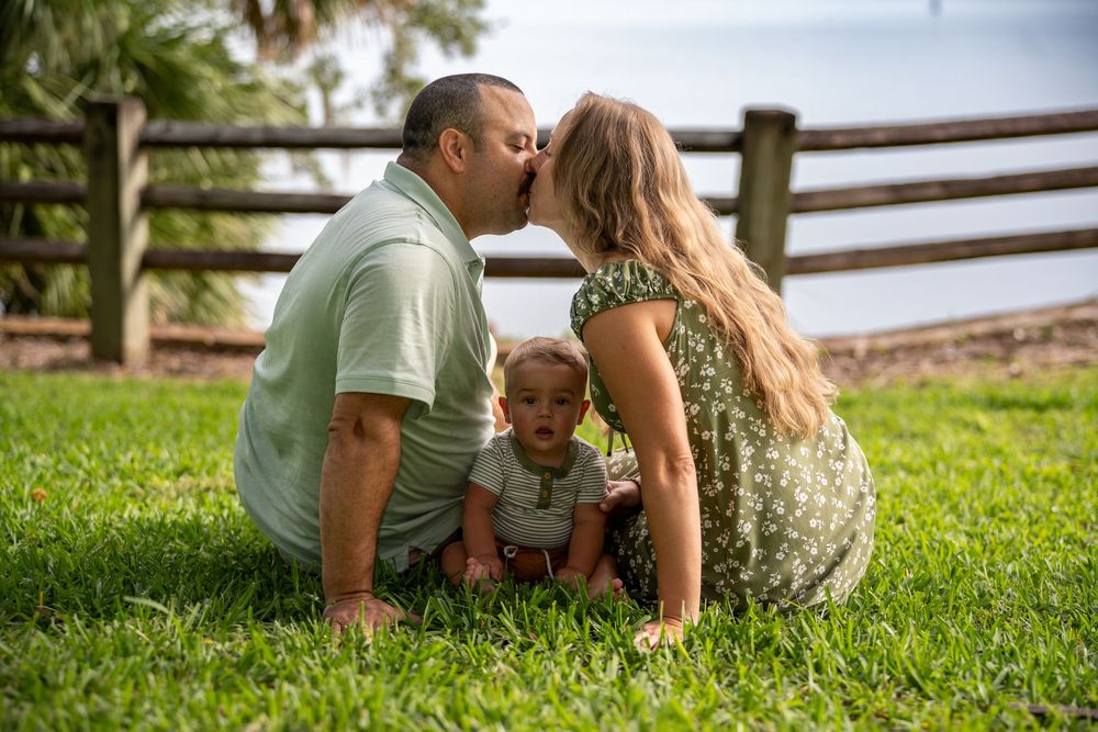 Family sitting together on grass by wooden fence, sharing sweet moment during outdoor photoshoot in Tampa, Florida.