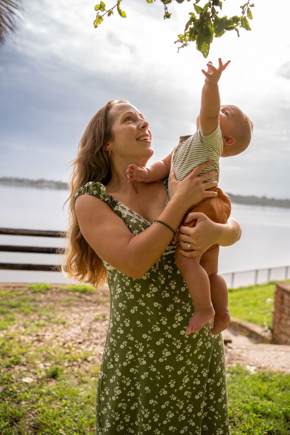 Mother lifting baby playfully by the water on a sunny day, outdoor family photoshoot in Tampa, Florida.
