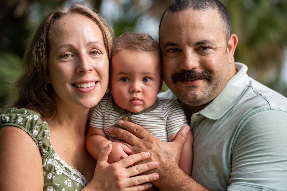 Loving family portrait in Tampa, Florida — parents smiling while holding baby in striped shirt, outdoor lifestyle photography.