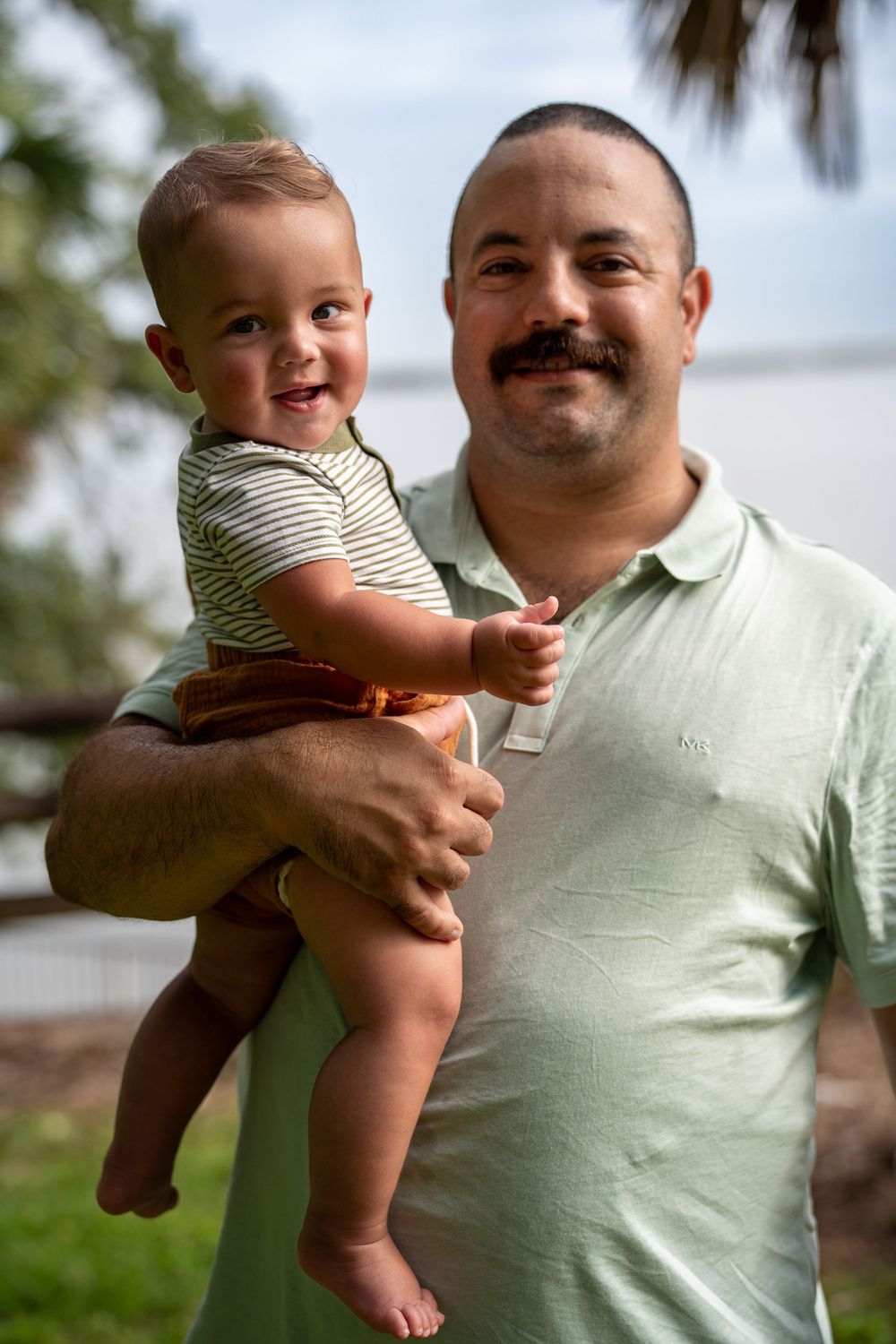 Father holding baby and laughing together outdoors in Tampa, Florida, natural candid family photography.