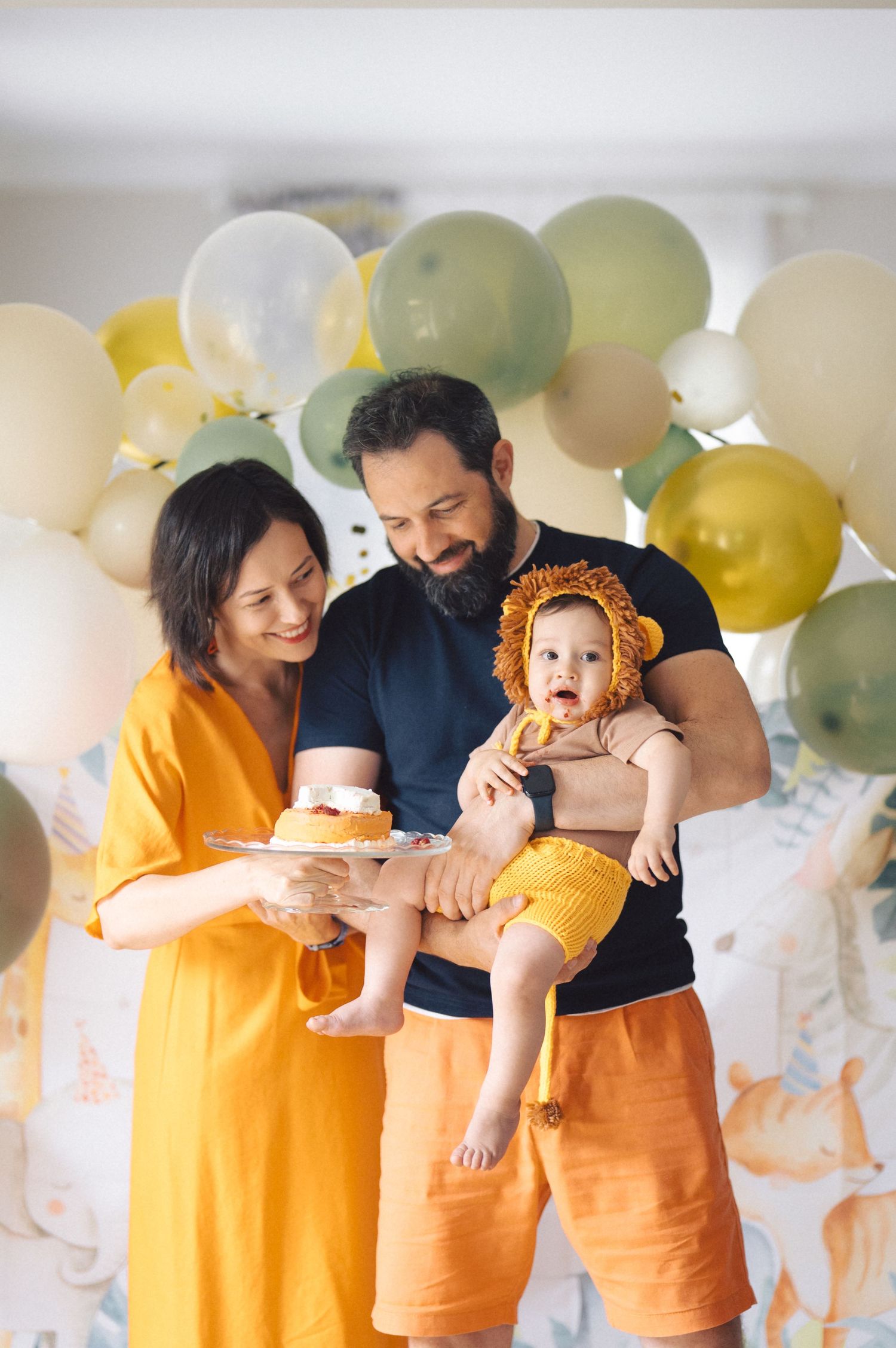 Family celebrates together against backdrop of yellow, green and white balloons in a bright indoor setting.