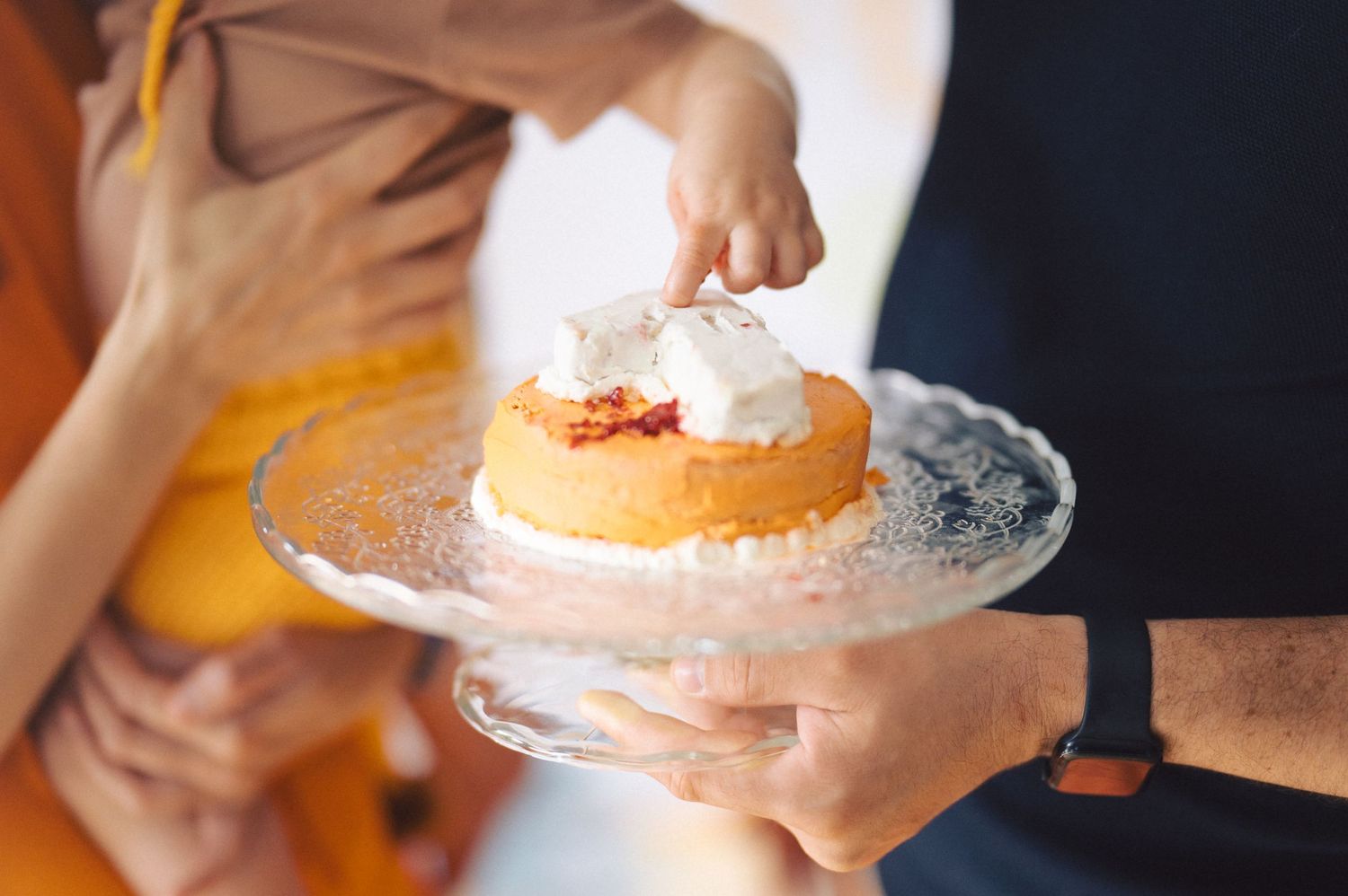 Close-up view of hands holding an elegant cake stand with a whipped cream topped dessert.
