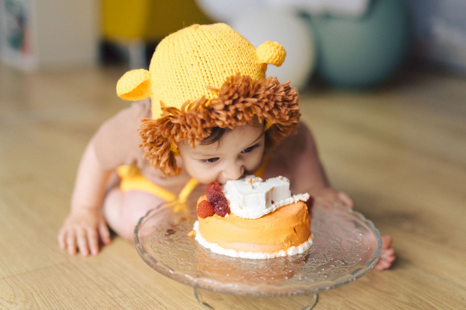 Baby with a bright yellow bow wearing a white dress smashes a chocolate cake during first birthday celebration.