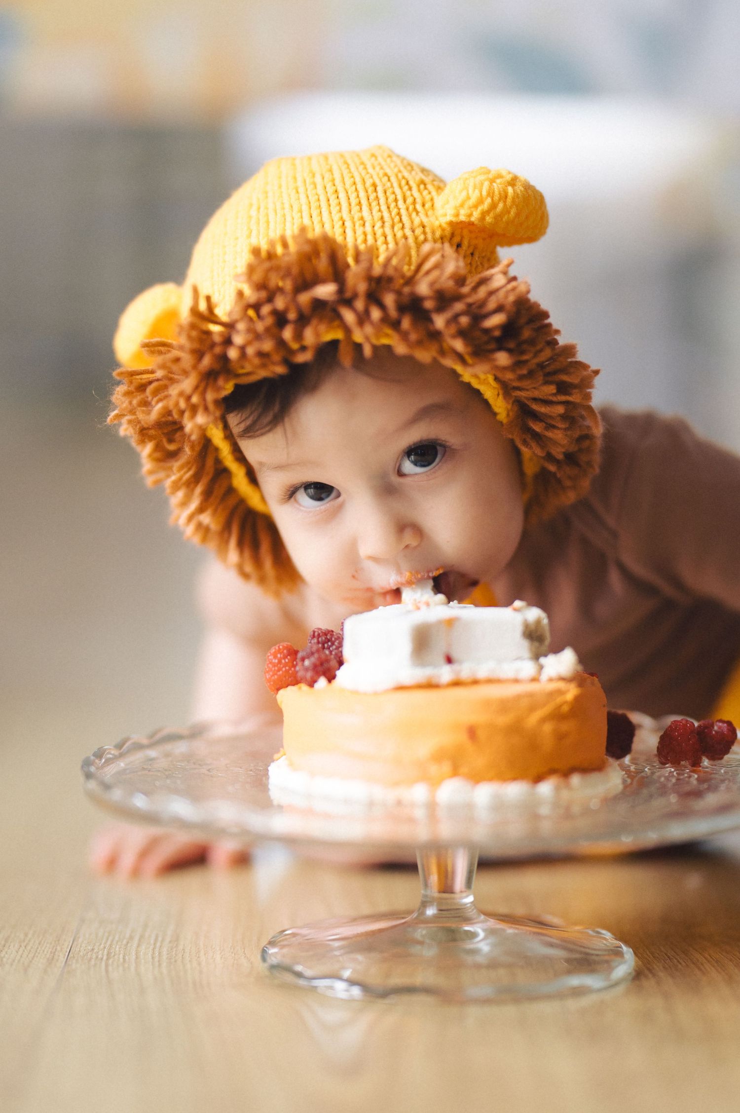 Series of photos showing someone in an orange knit hat peeking at and eating cake off a glass cake stand.