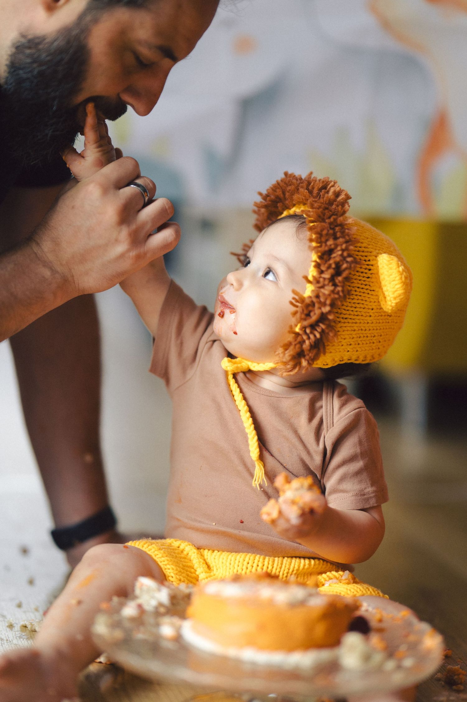 Sweet moment shared between adult and child in yellow knit hat while enjoying dessert at table.