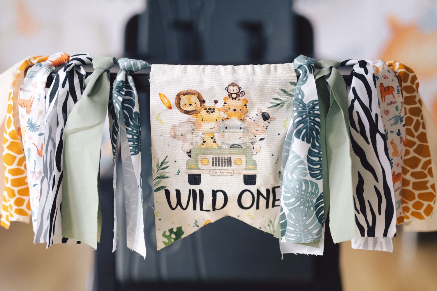 Safari themed 'Wild One' party banner with zebra and giraffe print fabric streamers and jungle animal decorations.