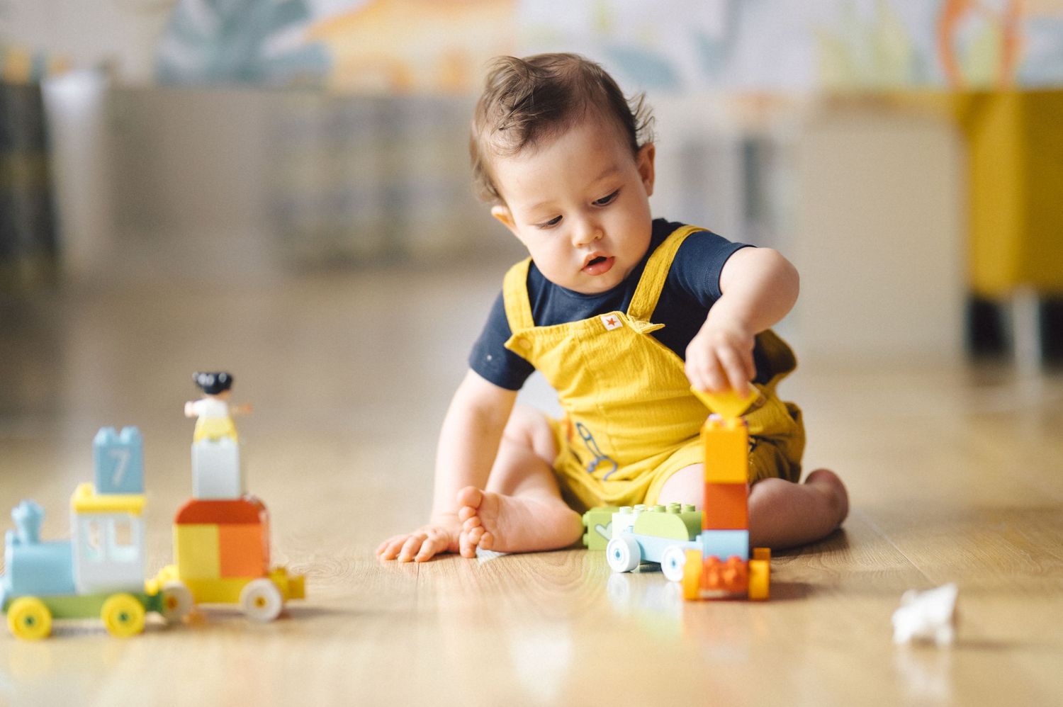 Child playing with colorful toy cars and vehicles on a wooden floor while developing motor skills.