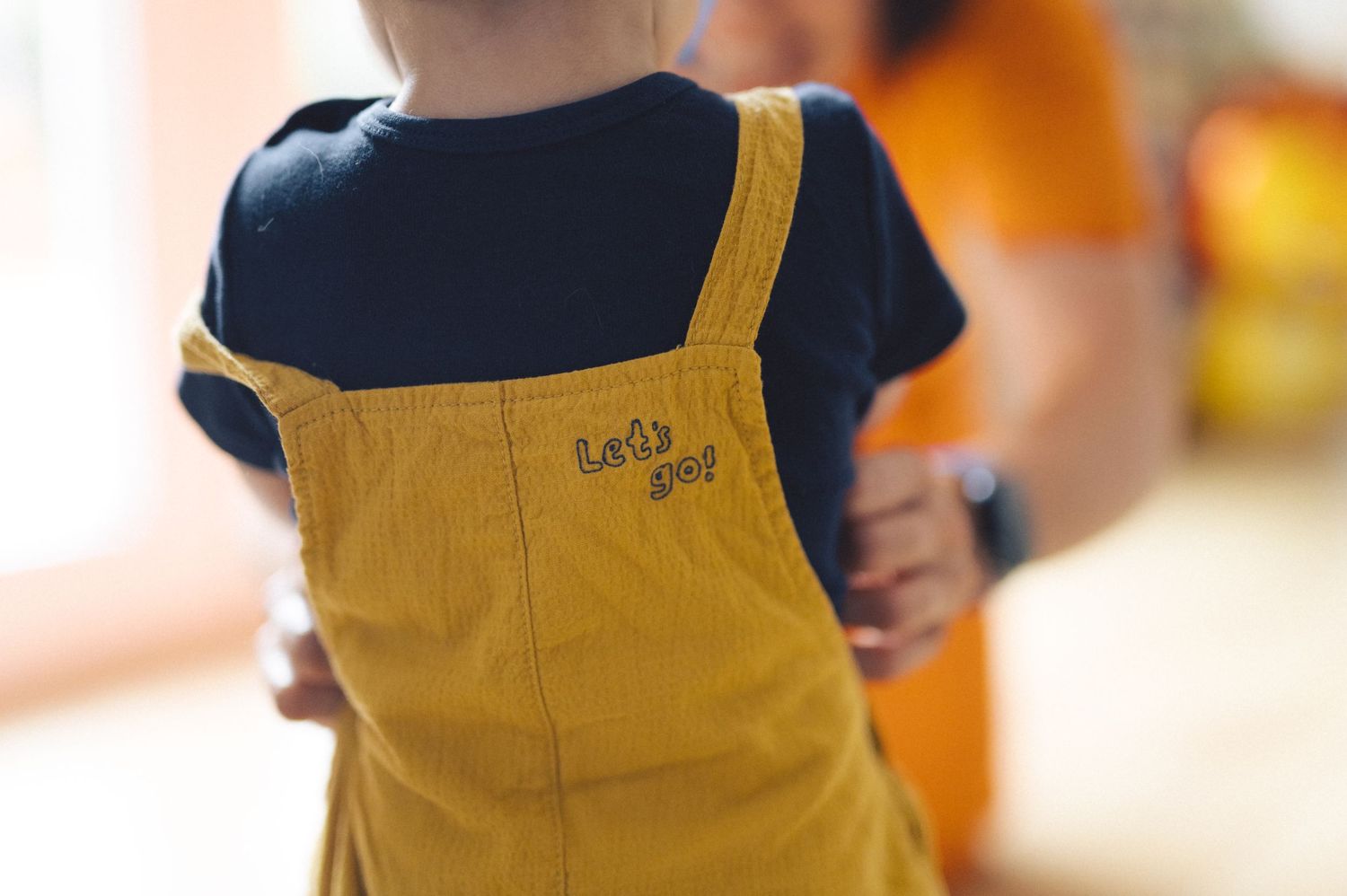 A person wearing yellow overalls is shown from behind walking with their hand in their pocket.