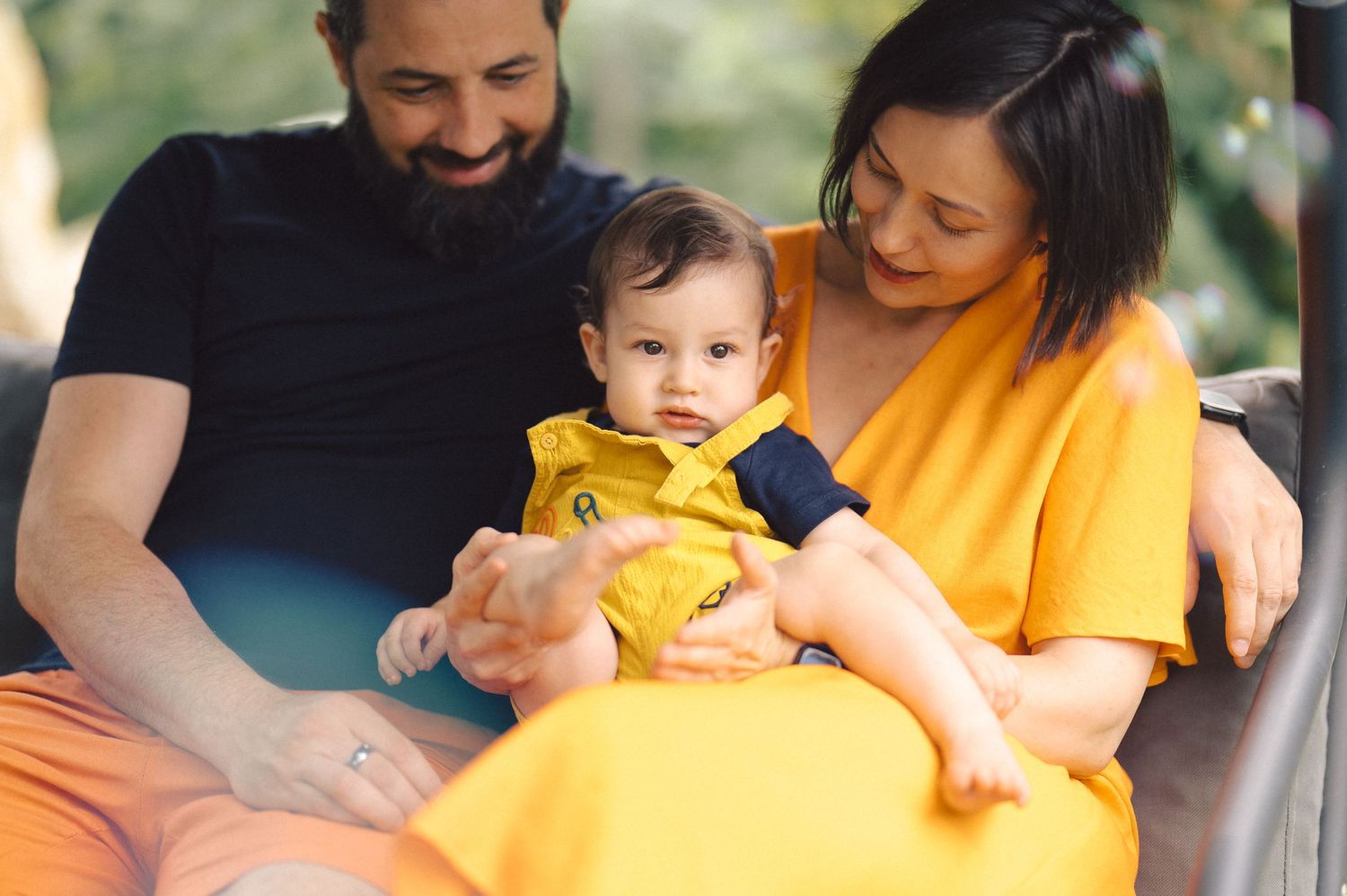 Family wearing yellow sits together outdoors sharing a tender moment with their baby.